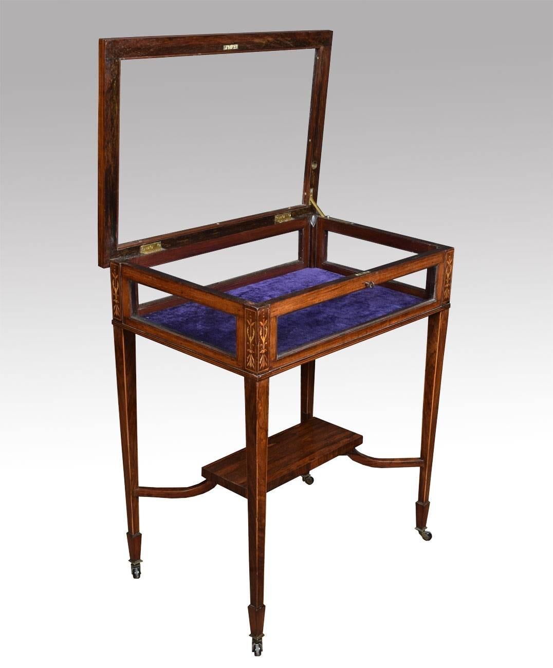 Edwardian rosewood and inlaid rectangular bijouterie display table, bordered with boxwood lines and decorated with foliate scroll designs, having a hinged glazed panel top and glazed panel sides all raised up on square tapered legs terminating in