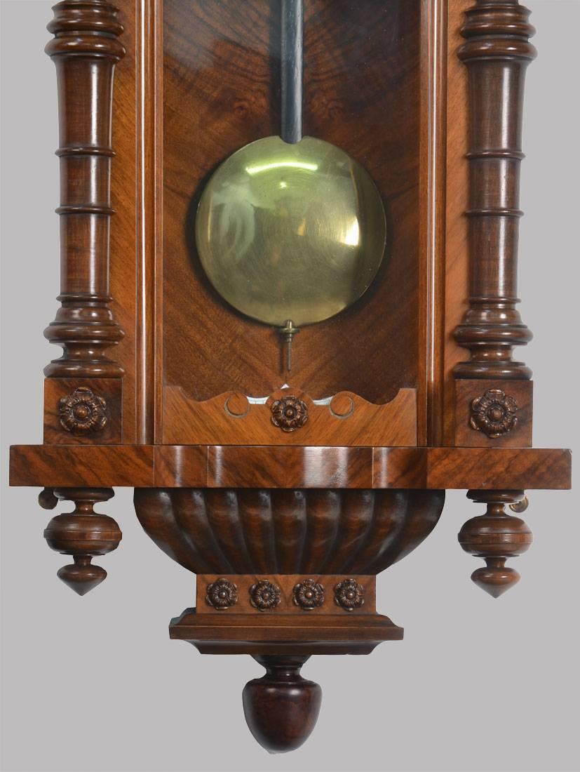 

Vienna regulator style wall clock, the case surmounted by moulded and finial pediment above a full length arched glazed door flanked by turned half columns enclosing a two-piece white enamel dial with Roman numerals and subsidiary seconds dial,