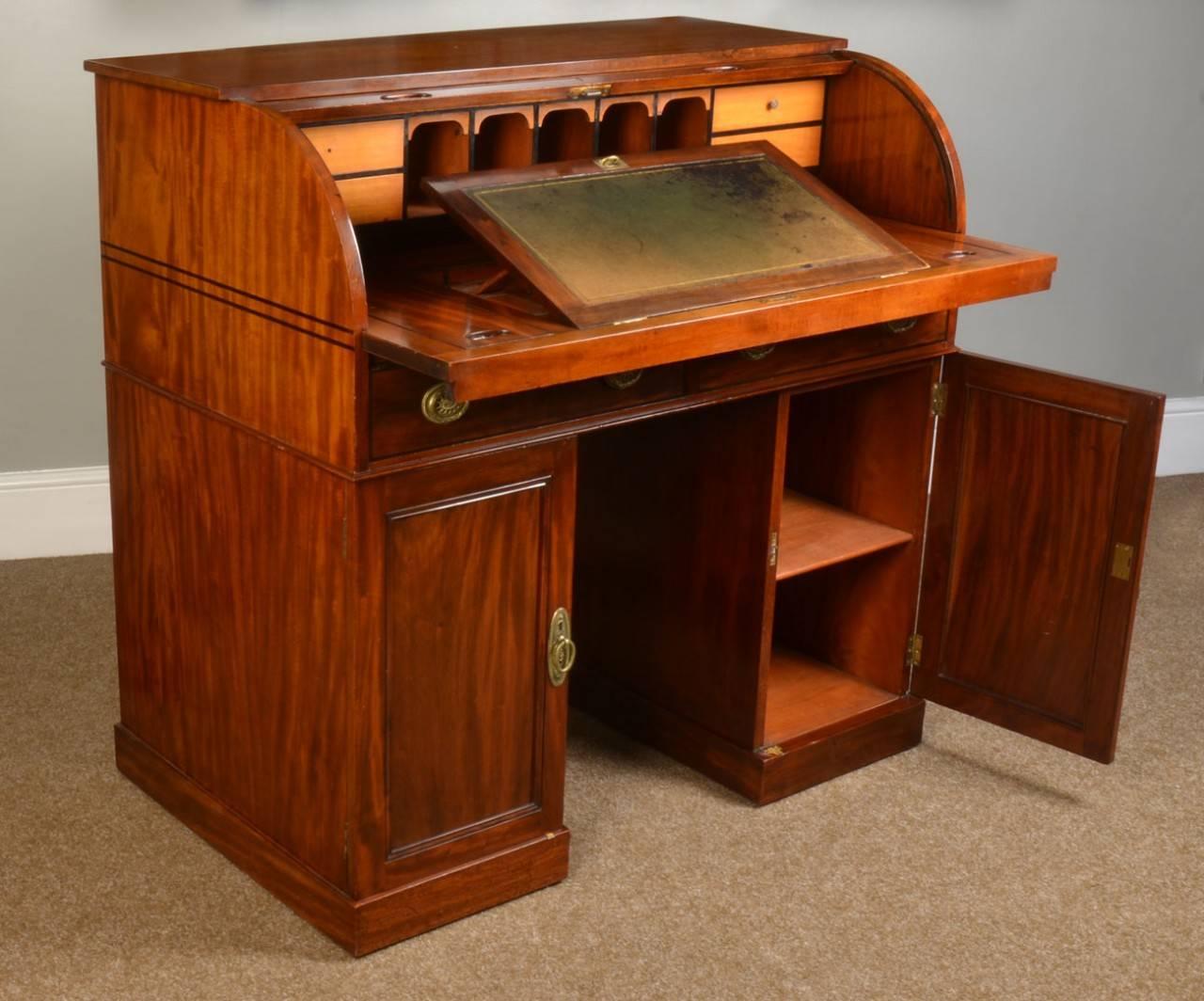 

A mahogany twin pedestal roll top desk, the solid mahogany ebony strung roll front enclosing an arrangement of pigeon holes and drawers with sliding leather writing surface, above two frieze drawers and kneehole flanked by two mahogany panel