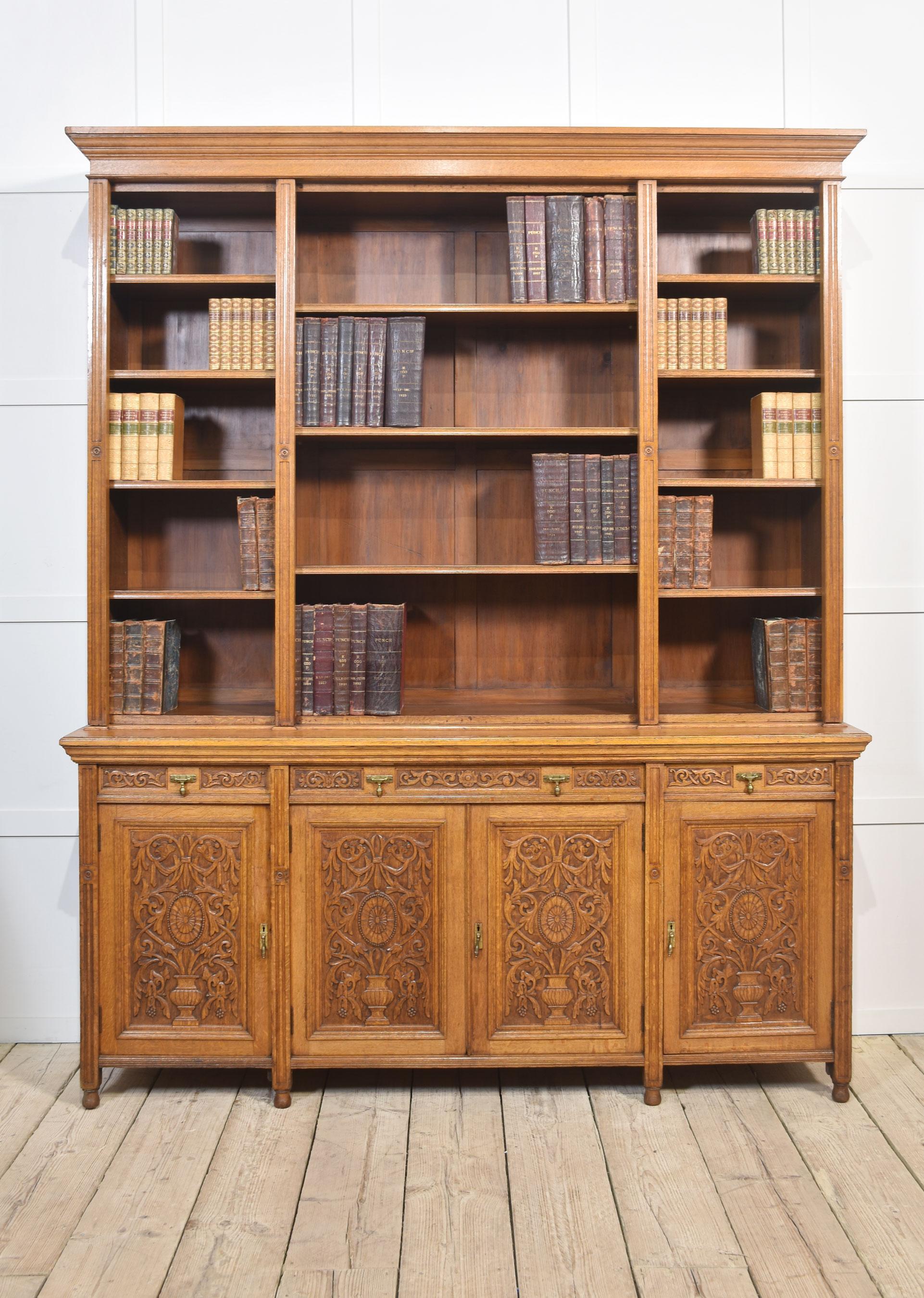 Libreria in rovere del XIX secolo con cornice svasata su tre ampie campate di ripiani regolabili. La base è dotata di un cassetto lungo e due cassetti corti con maniglie in ottone. Sopra quattro porte ben intagliate e canalate con dettagli di urne e