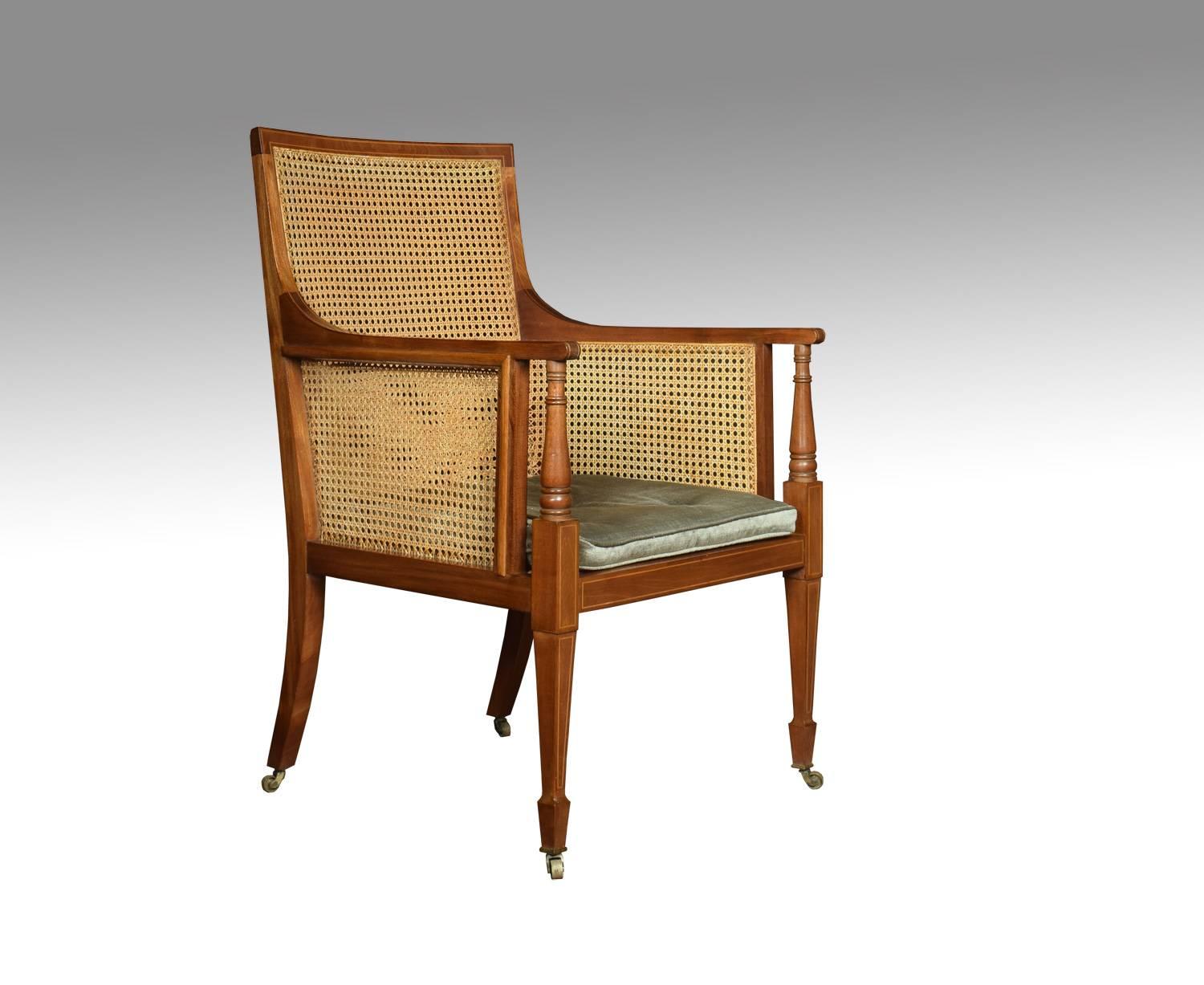 Edwardian string inlaid armchair, with solid mahogany frame and inset bergere back and seat with removable buttoned cushion. Raised up on tapering legs and spade feet. Terminating in brass caps and castors.

Dimensions:
Height 39 inches, height