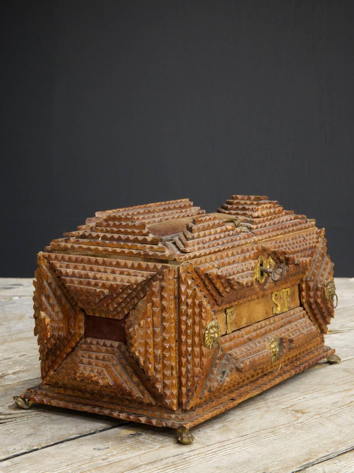 A spectacular example of tramp art.

The multi layered chip carved exterior having brass embellishments to the escutcheon, drawer pulls and hairy paw feet.

The top opens to reveal a floral paper liner and two small lidded compartments,