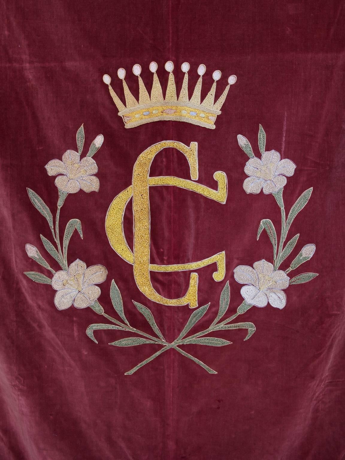 A red velvet banner with embroidered decoration.

The central C G monogram surrounded by lilies with crown above.

Late 19th century.
  