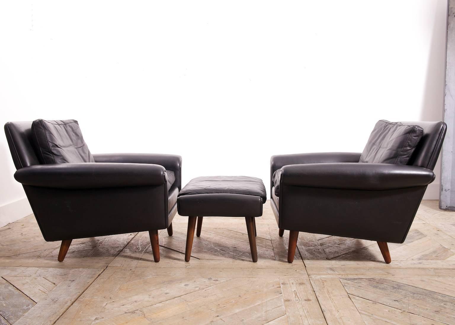 A pair of black leather armchairs with ottoman en suite.

Designer Aage Christiansen for the Diplomat range by Erhardsen & Andersen, 1965.

Superb quality, down cushions and raised on solid rosewood tapering legs.

Price is for the set ( two chairs