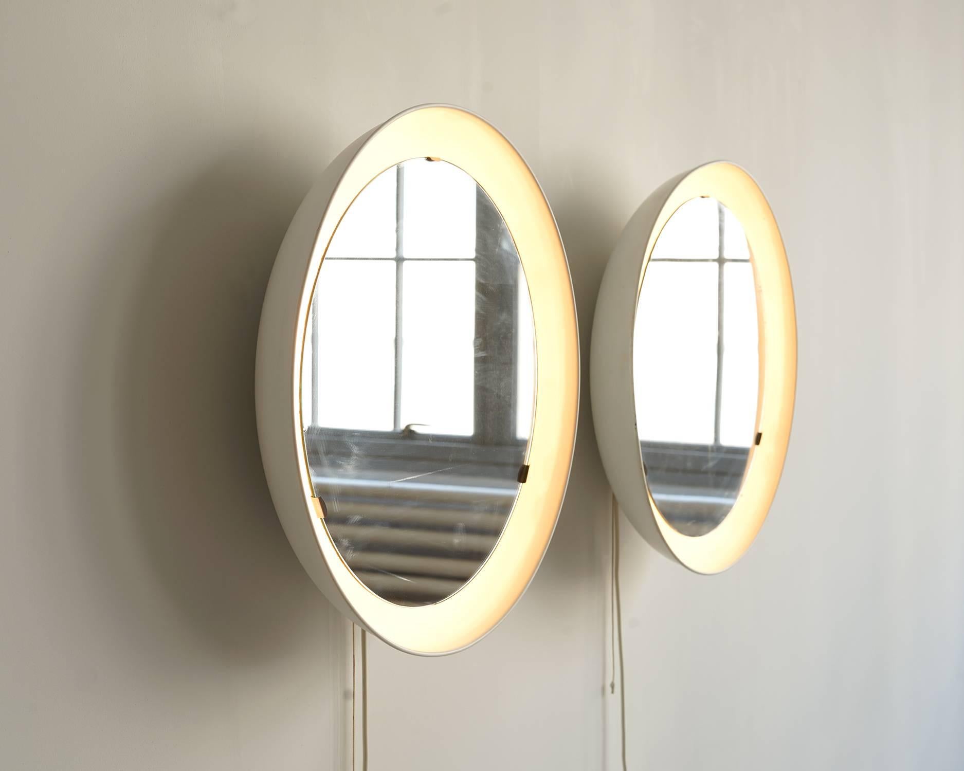 A great pair with original mirrored glass floating in white, concave, metal frames. Recessed lights behind the glass illuminate and frame your reflection in a warm glow. Original cord with plug and pull cord switch; may also be easily hard wired