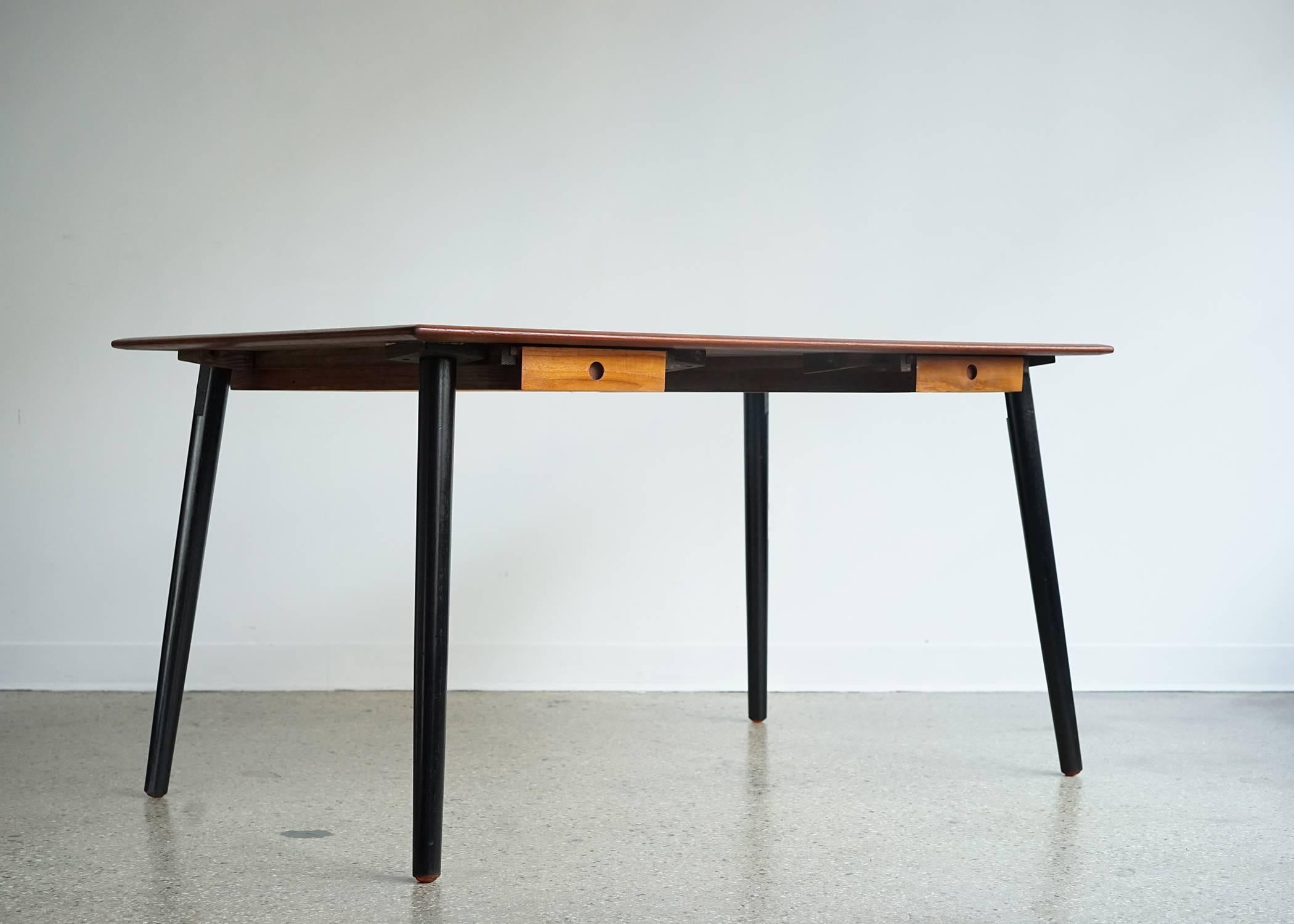 Teak top with drawers on either side elevated on ebonized tapered legs. With the legs set at the four corners, it functions as a partners desk or a dining table in the middle of a room. Two legs can be repositioned between the drawers for a more