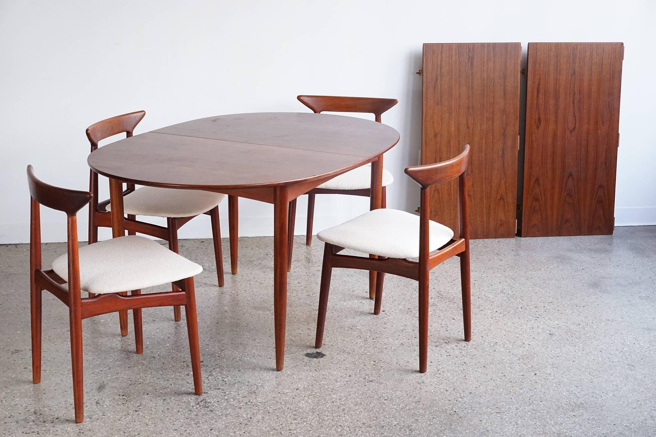 Teak set including four chairs, oval dining table and two leaves. Compact for daily use with both leaves removed; seats eight comfortably with both leaves in place, seats six with one leaf, seats four with no leaves. Original finish with warm tone