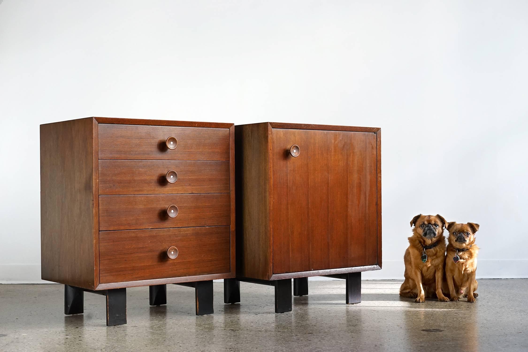 Handsome, versatile pair in all original vintage condition with rich tone and natural patina. Distinctive "cupcake" pulls, walnut veneer, ebonized legs, four drawers, one adjustable shelf, original finish. Label inside top drawer. Made in