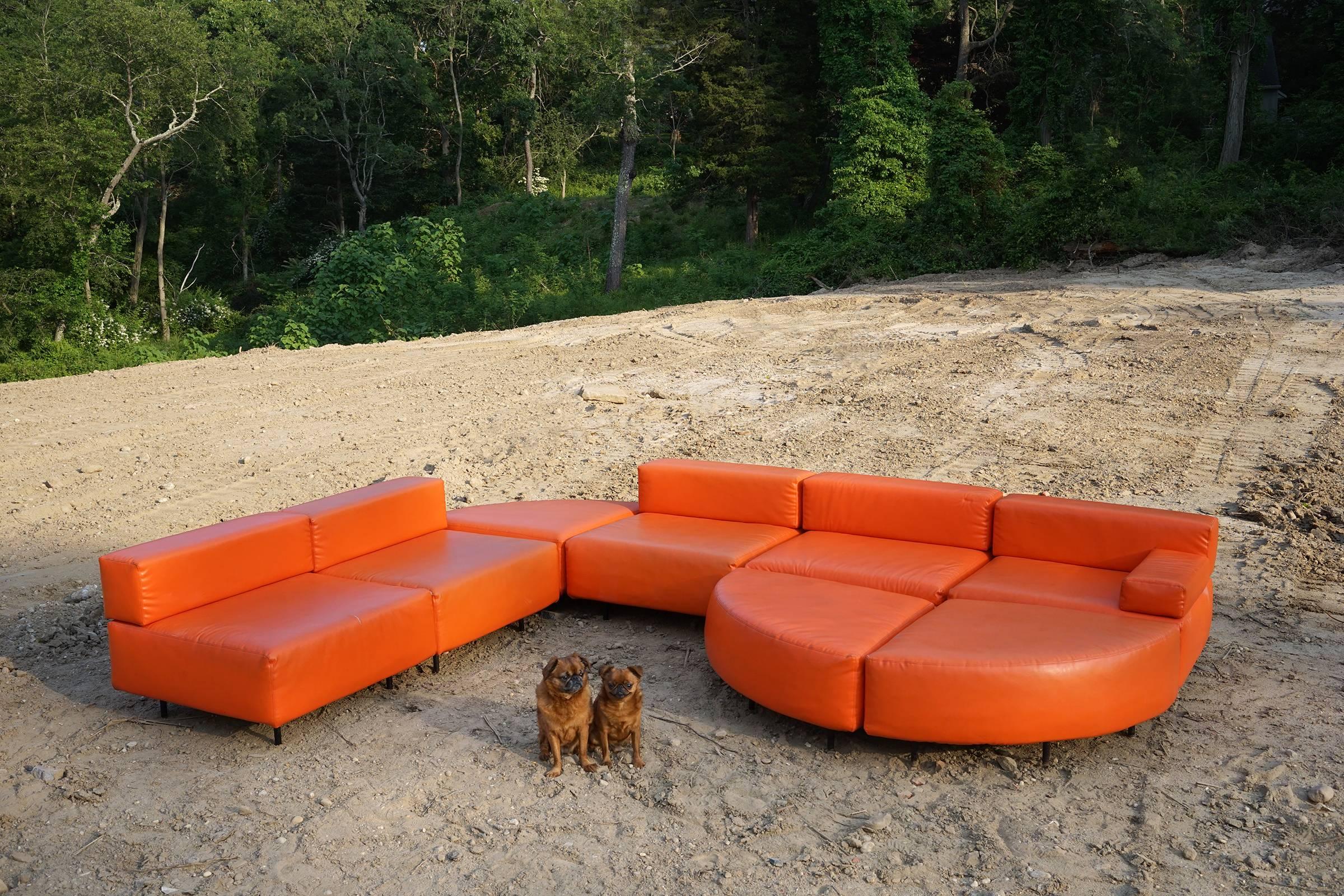 All original eight piece sectional in bright, orange leatherette upholstery, elevated on black tubular legs. Each section measures 32 inches square.

