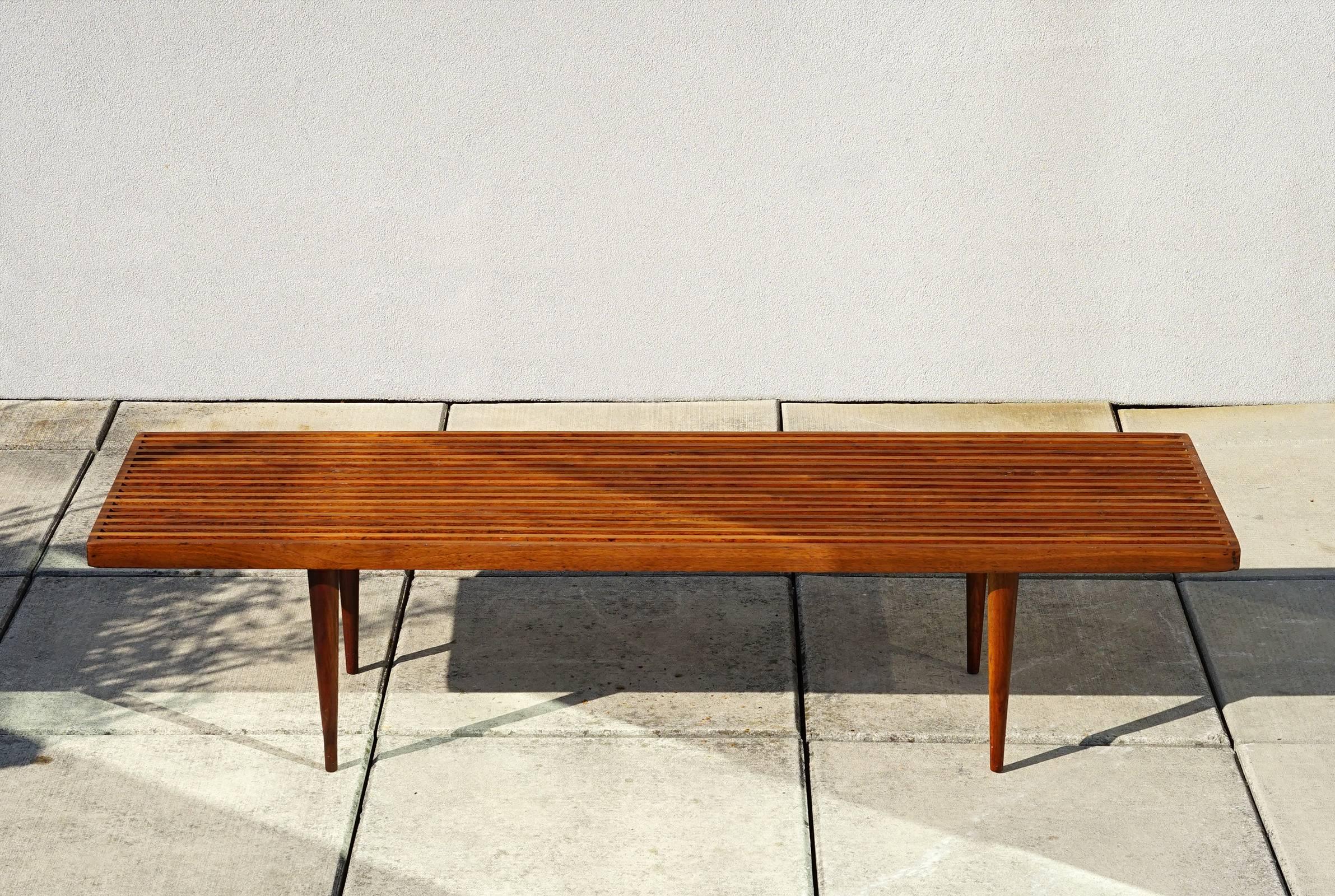 5 feet long. Light and airy design with its long, tapered legs, slender slats, and cantilevered top. Solid American walnut components. Original 1950s production. Legs screw off without tools for easy transport or storage. Handsome and versatile as a