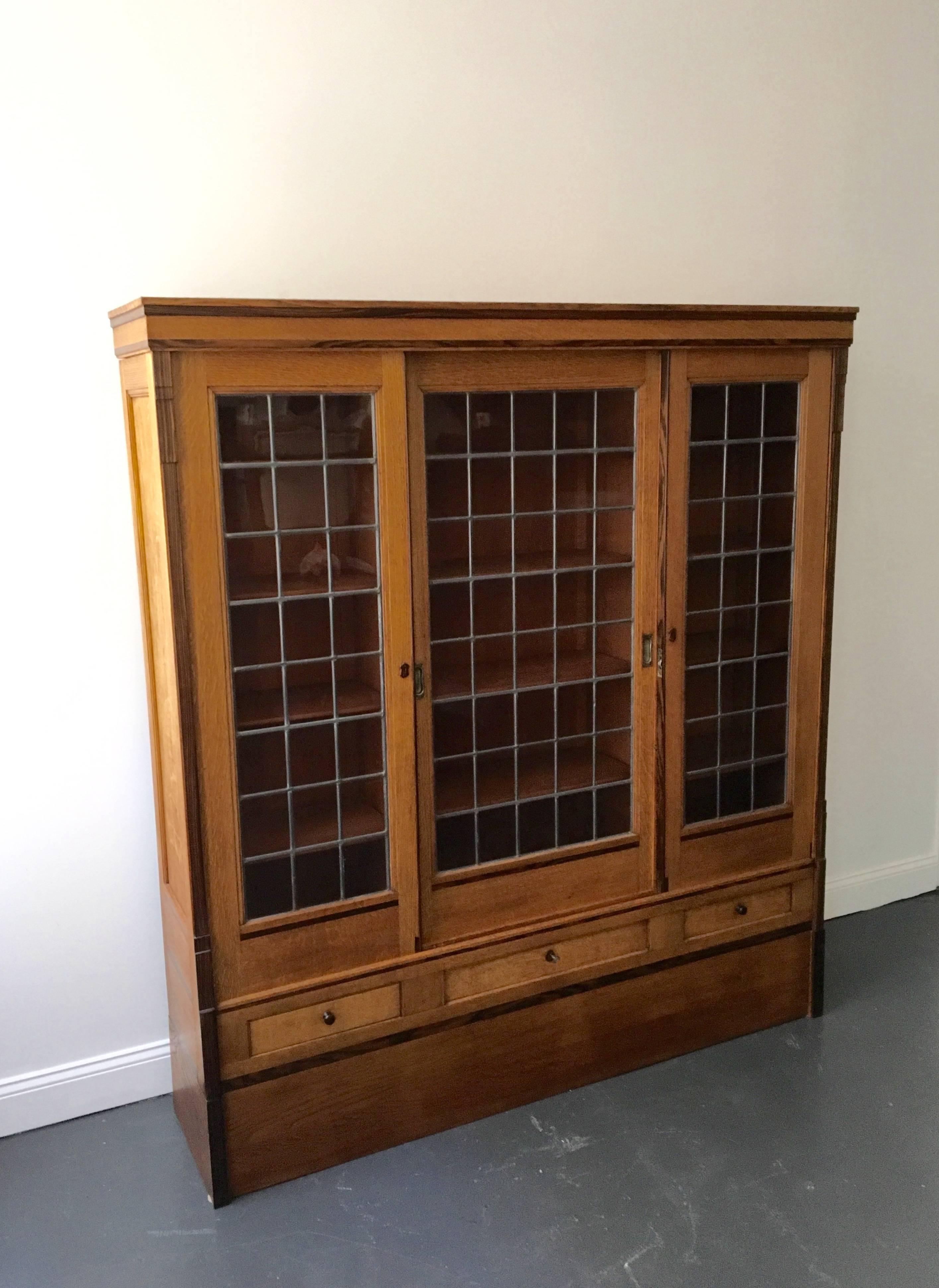 A circa 1930s cabinet in oak, Macassar and glass. Three sliding doors with internal shelves and three lower drawers.