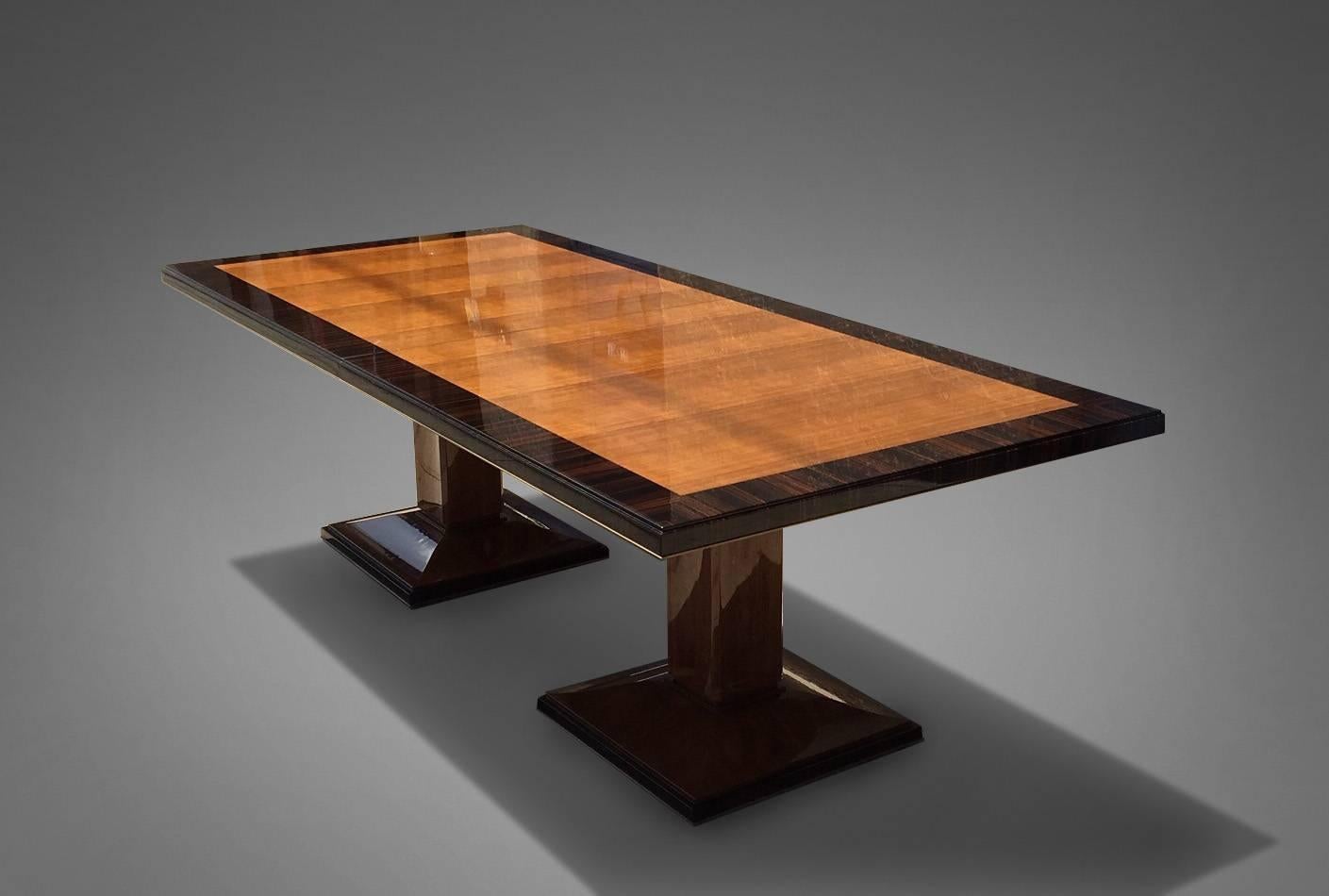 Dining table with a double pedestal base in Macassar ebony, top in walnut with a large band of Macassar ebony and bronze detail around edge. The dining table opens to include a single leaf. Measures: Table 96