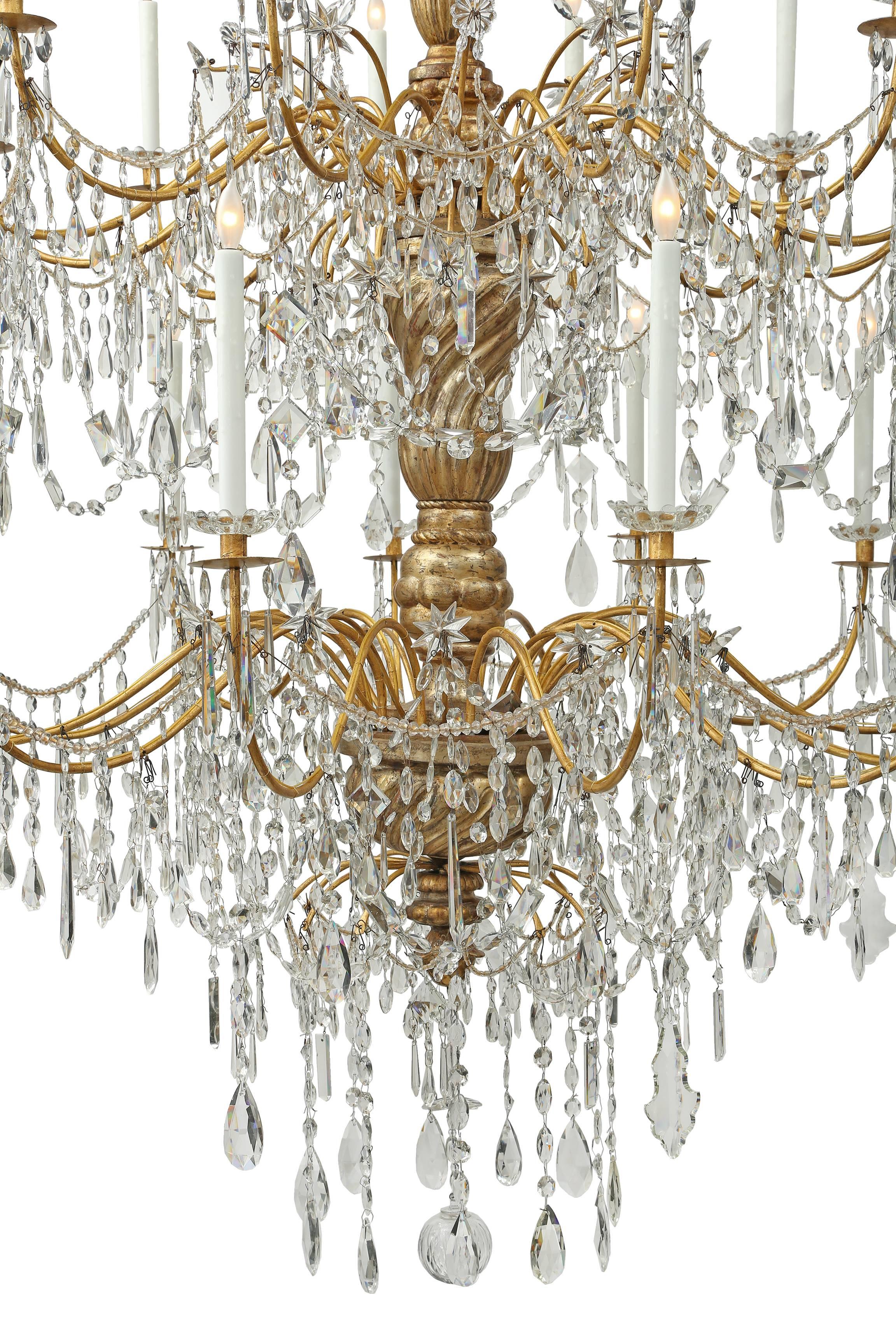 A palatial Italian 18th century Genovese twenty four light, two tier chandelier. This monumental chandelier is centered by an elegant hand blown glass ball encircled by cut crystal pendants. Each tier displays twelve S scrolled gilt metal arms with