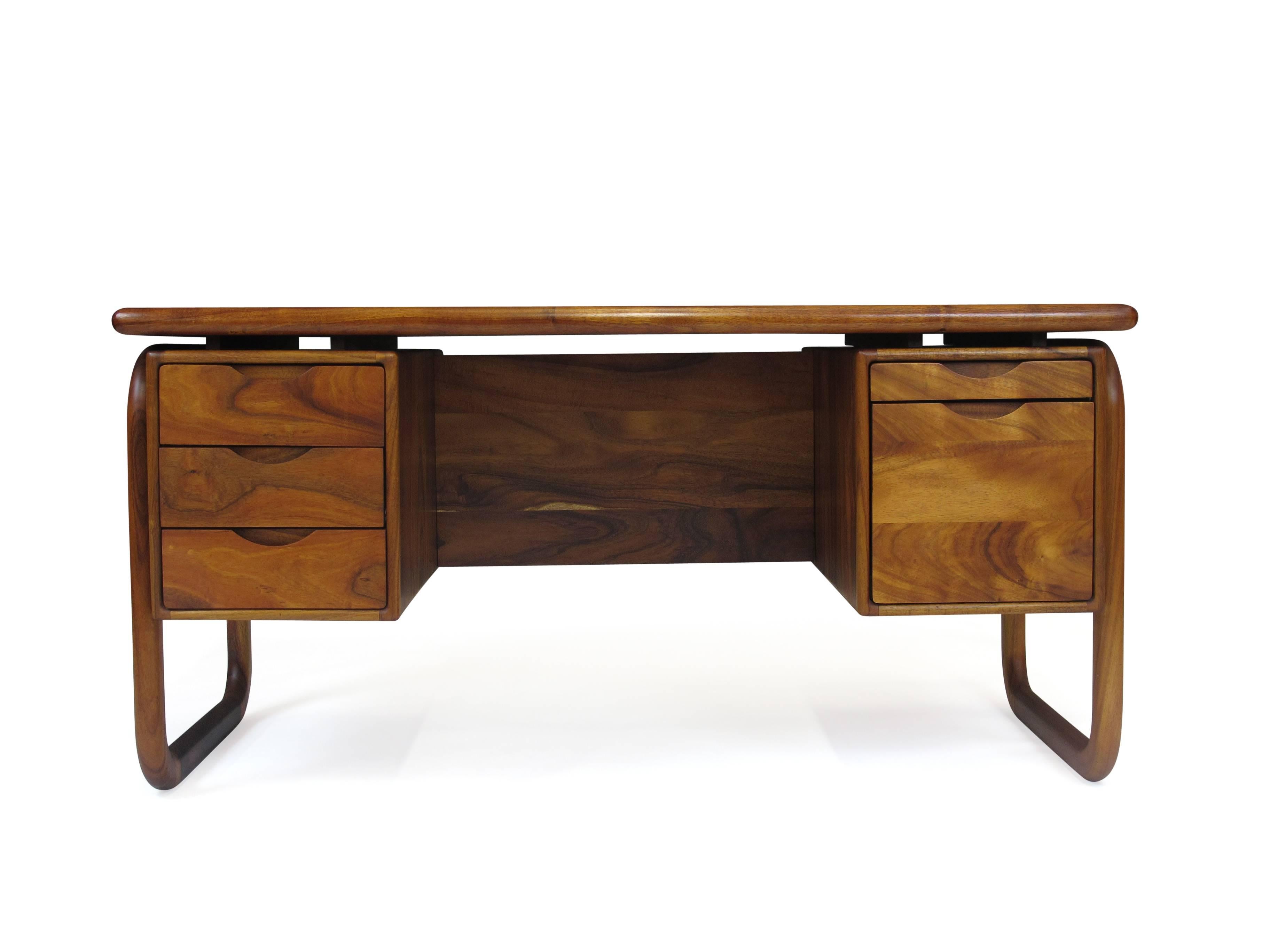 Desk finely handcrafted of solid koa wood with rich grain on sculpted legs and floating top surface. Two drawers on the right including one filing cabinet and three drawers on the left side. Finished back and with two bookcases. Professionally