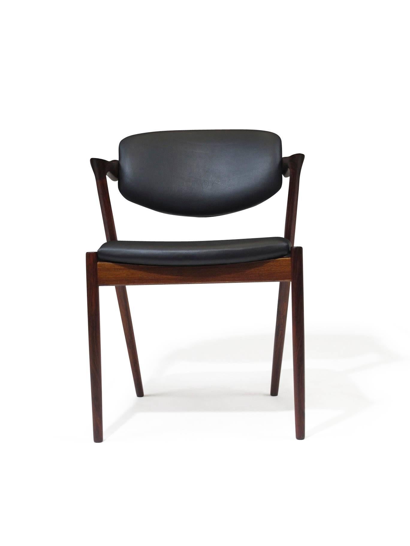 Kai Kristiansen, model #42 dining chairs for V. Schou Andersen crafted of dark Brazilian rosewood with tilting backrest and dramatic angled half armrest. Wood frame seat construction with new rubber straps covered in foam and new matte black