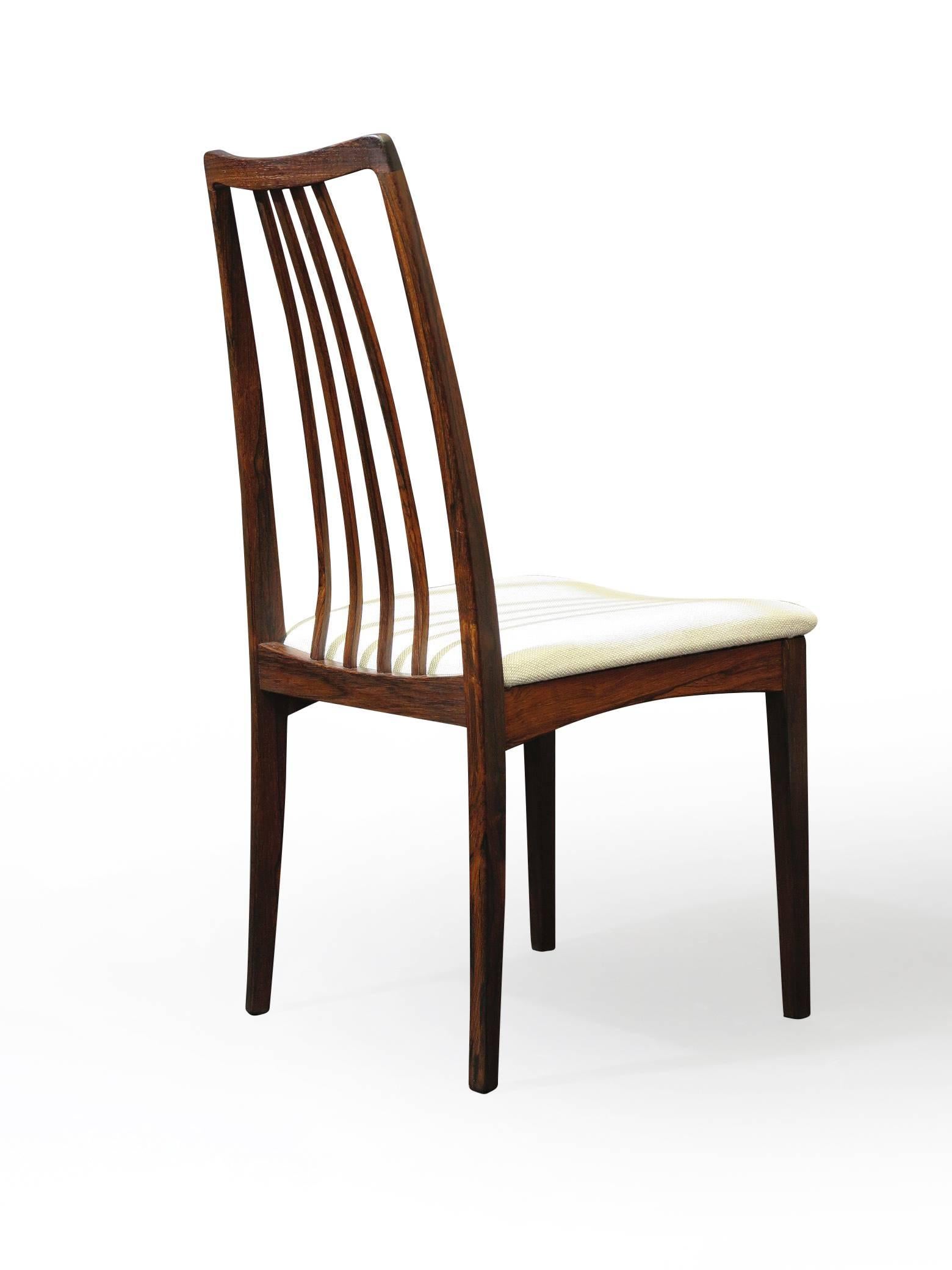 Six mid century Brazilian Rosewood dining chairs designed by Kofoed Larsen. Dark grain with elegant spindle back rests and newly upholstered seats in an off-white wool textile.