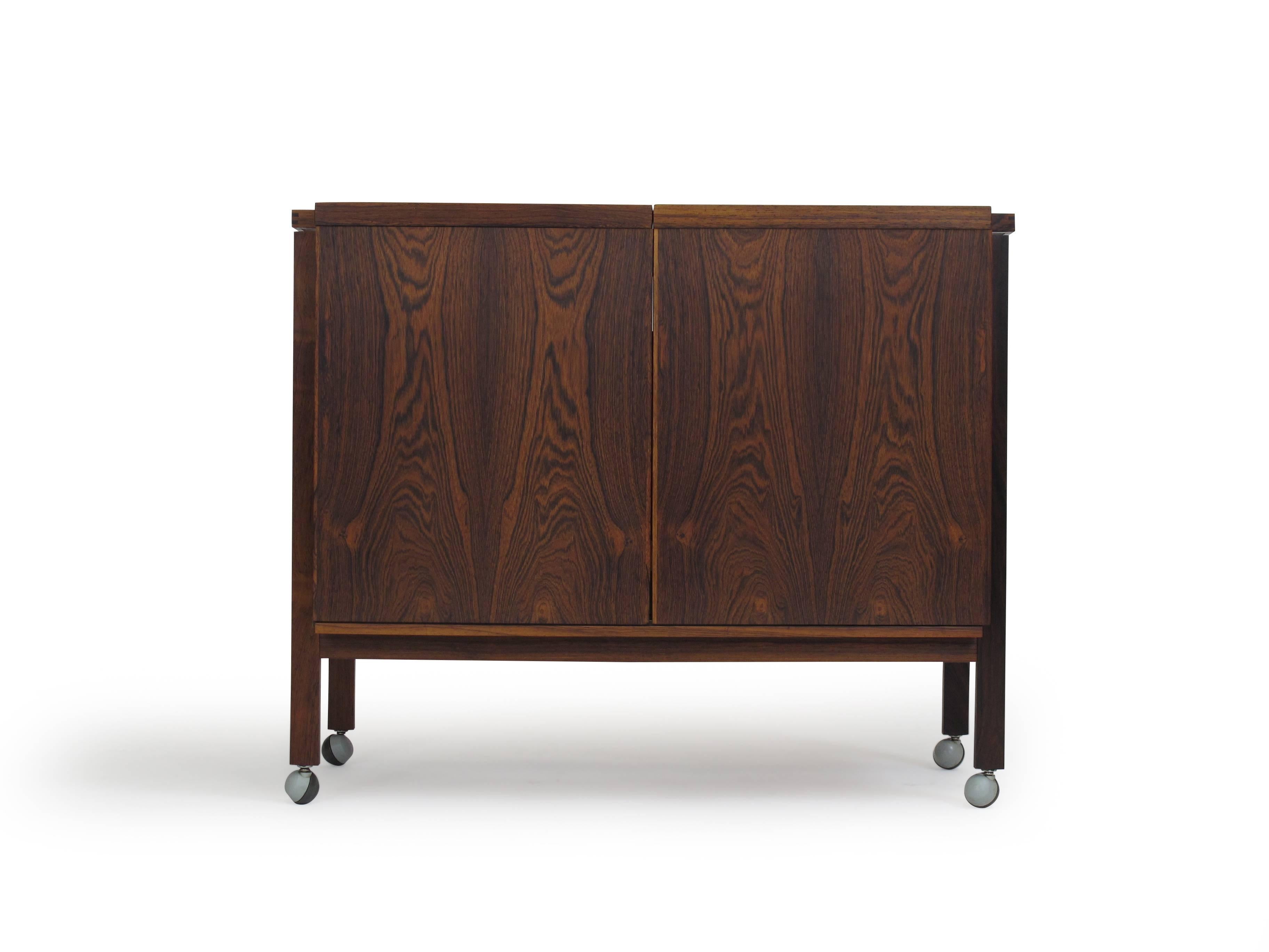 Niels Erik Glasdam Jensen expanding midcentury rosewood bar cabinet with two sections that slide out to reveal a stylish interior with a glass shelf above bottle storage with white sliding dividers. White laminated top for mixing drinks. Cabinet