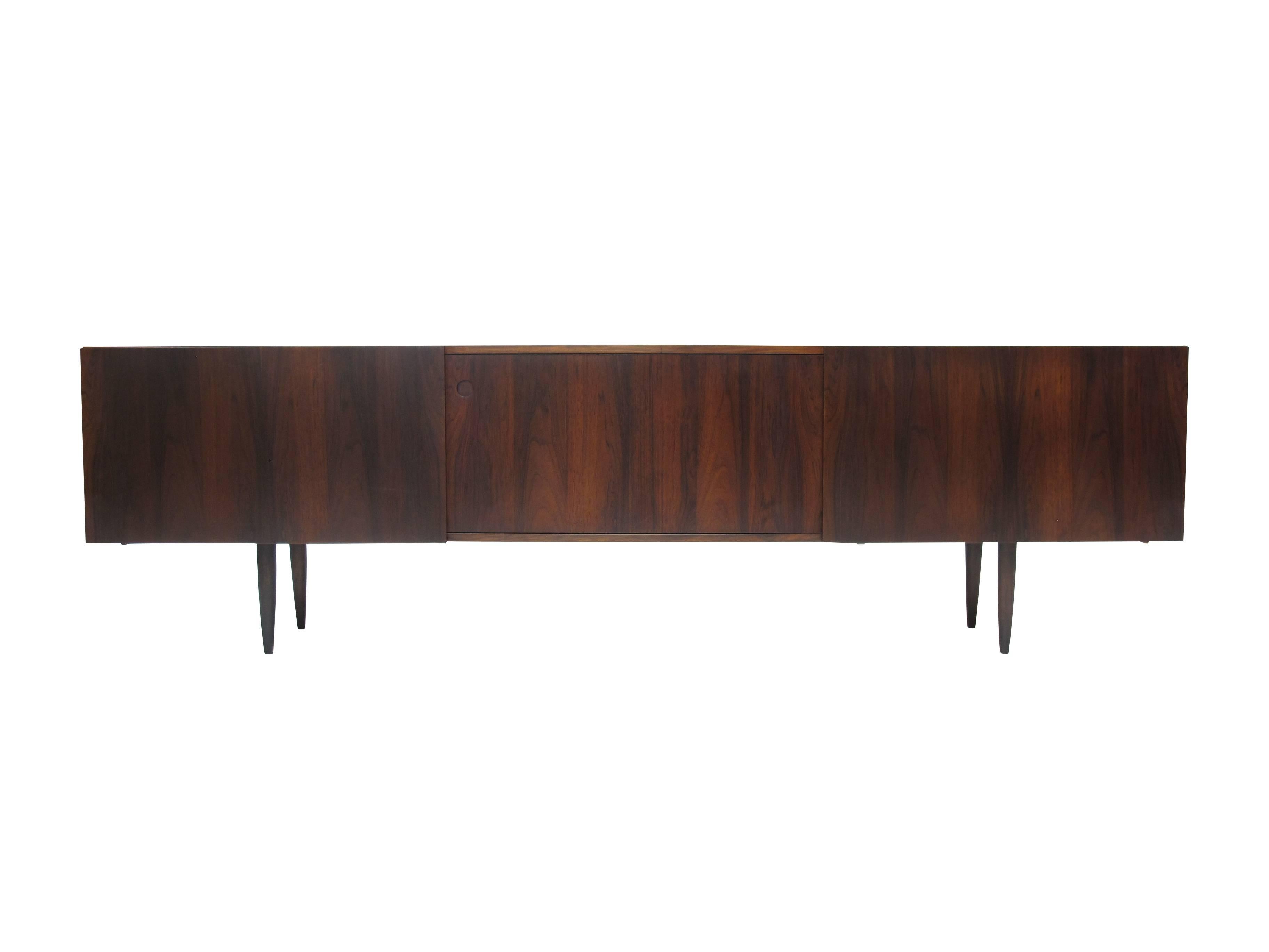 Brazilian rosewood credenza designed by Ib Kofod Larsen. Minimalist Danish design features three sliding doors raised on tapered legs. White oak interior with adjustable shelves and two drawers center. 