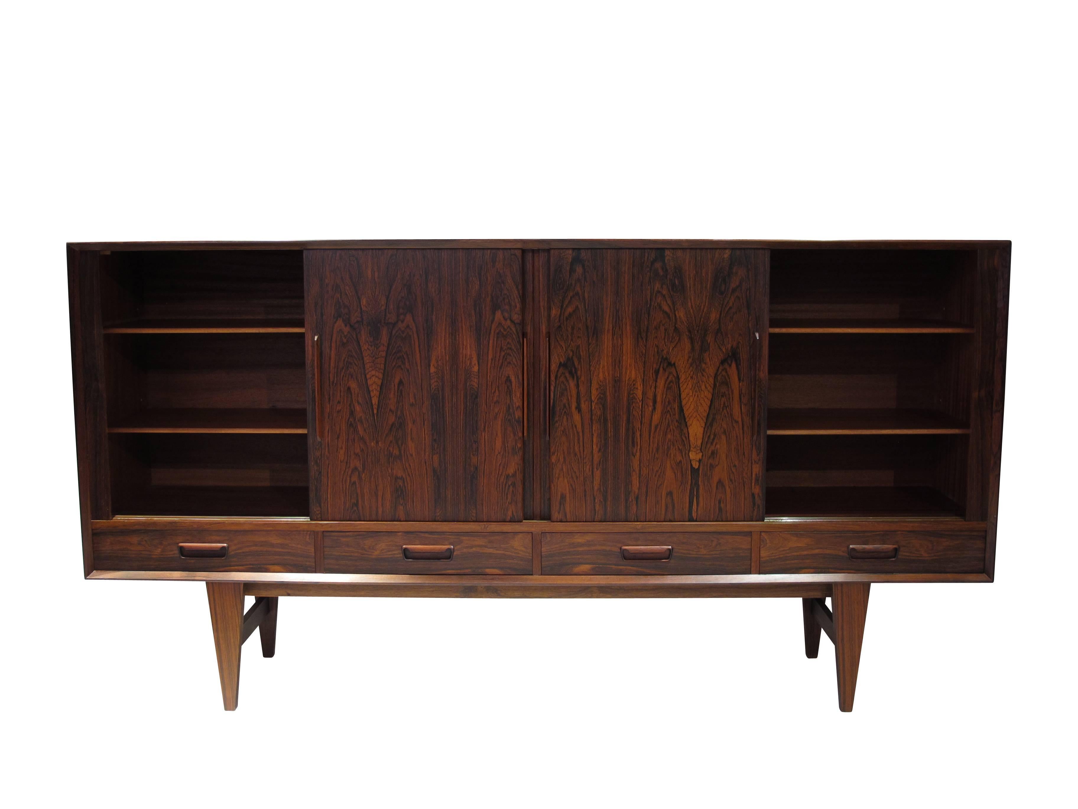 Mid-Century Rosewood sideboard with dynamic book-matched grain on four sliding doors. Interior has adjustable shelves on right and left. A light automatically turns on when center doors open, to reveal a mirrored bar with pull-out shelf and series