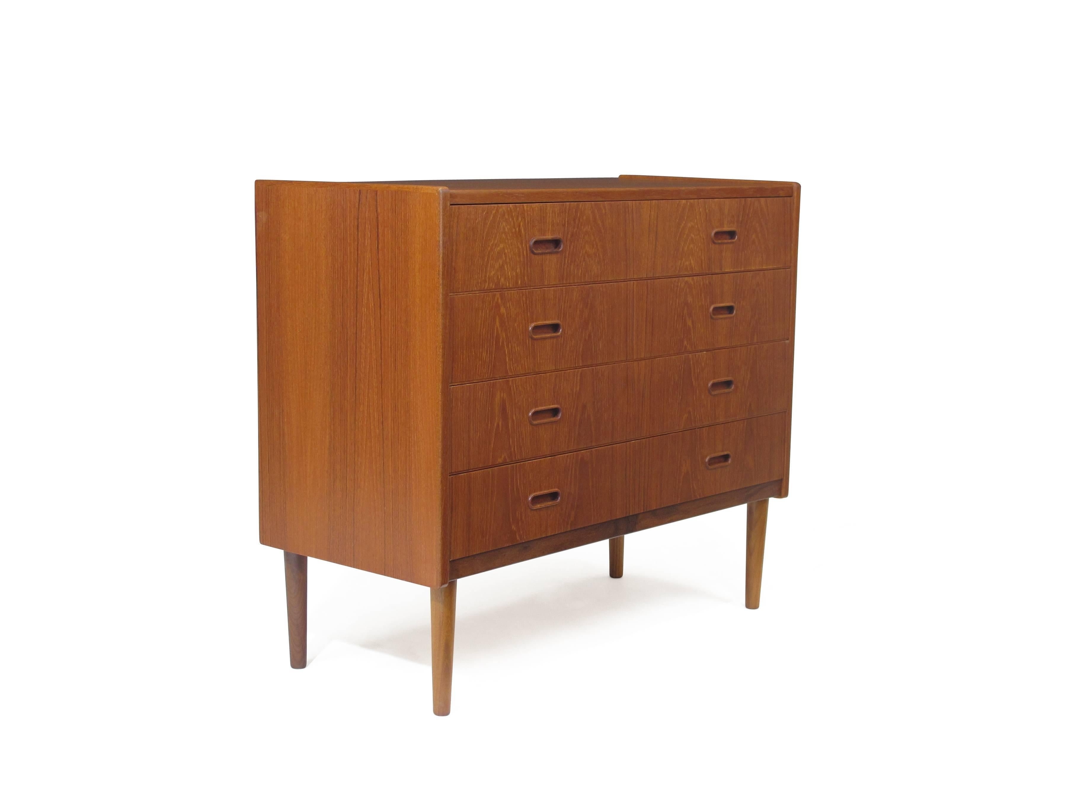 Midcentury four-drawer teak dresser with carved inset pulls, bookmatched graining, and solid turned tapered legs.