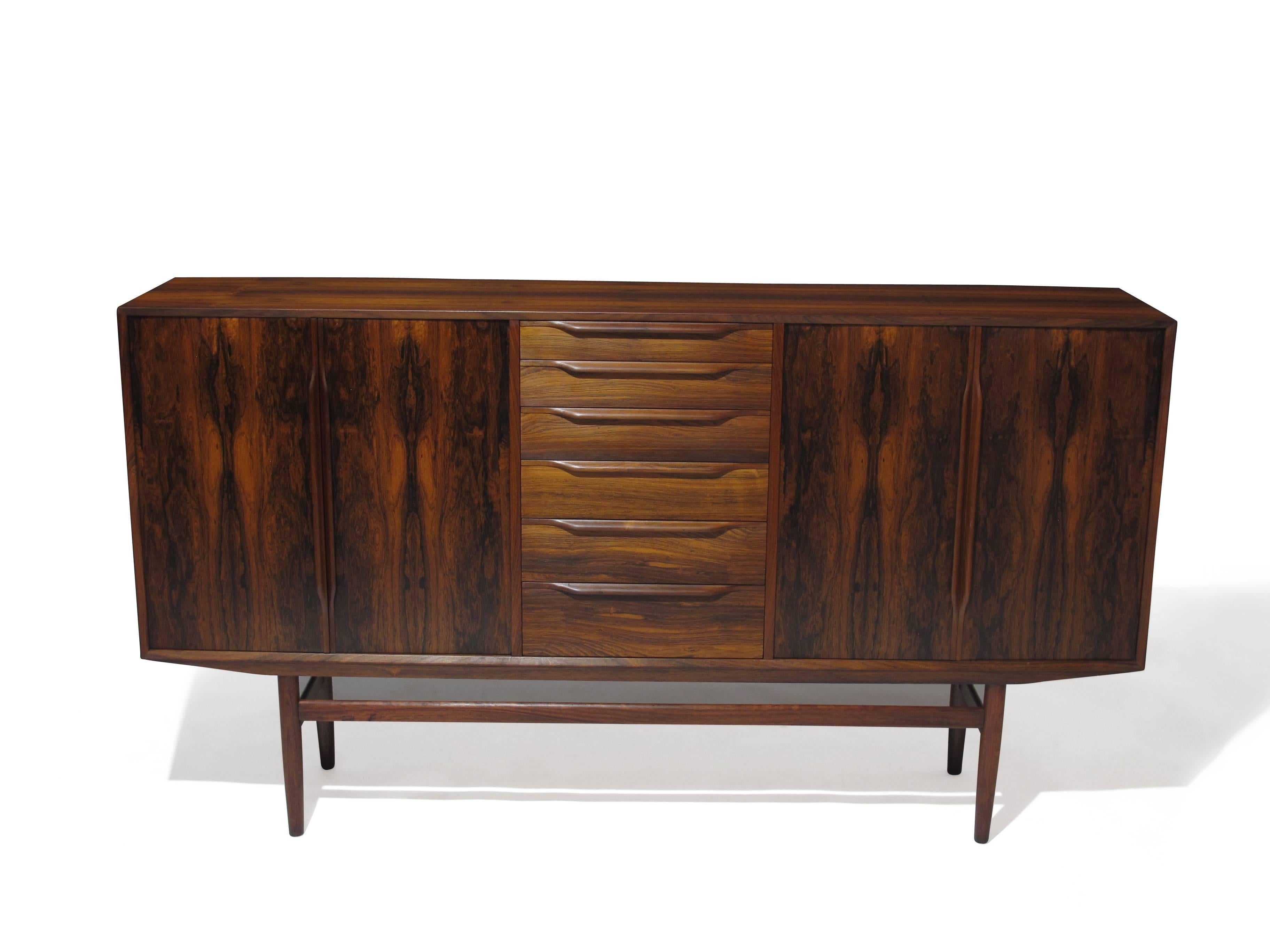 Danish credenza handcrafted of rosewood with book-matched graining, carved pulls and solid turned legs and stretchers. Centre section contains six drawers increasing in capacity from top to bottom. The outer door double door sections contain three