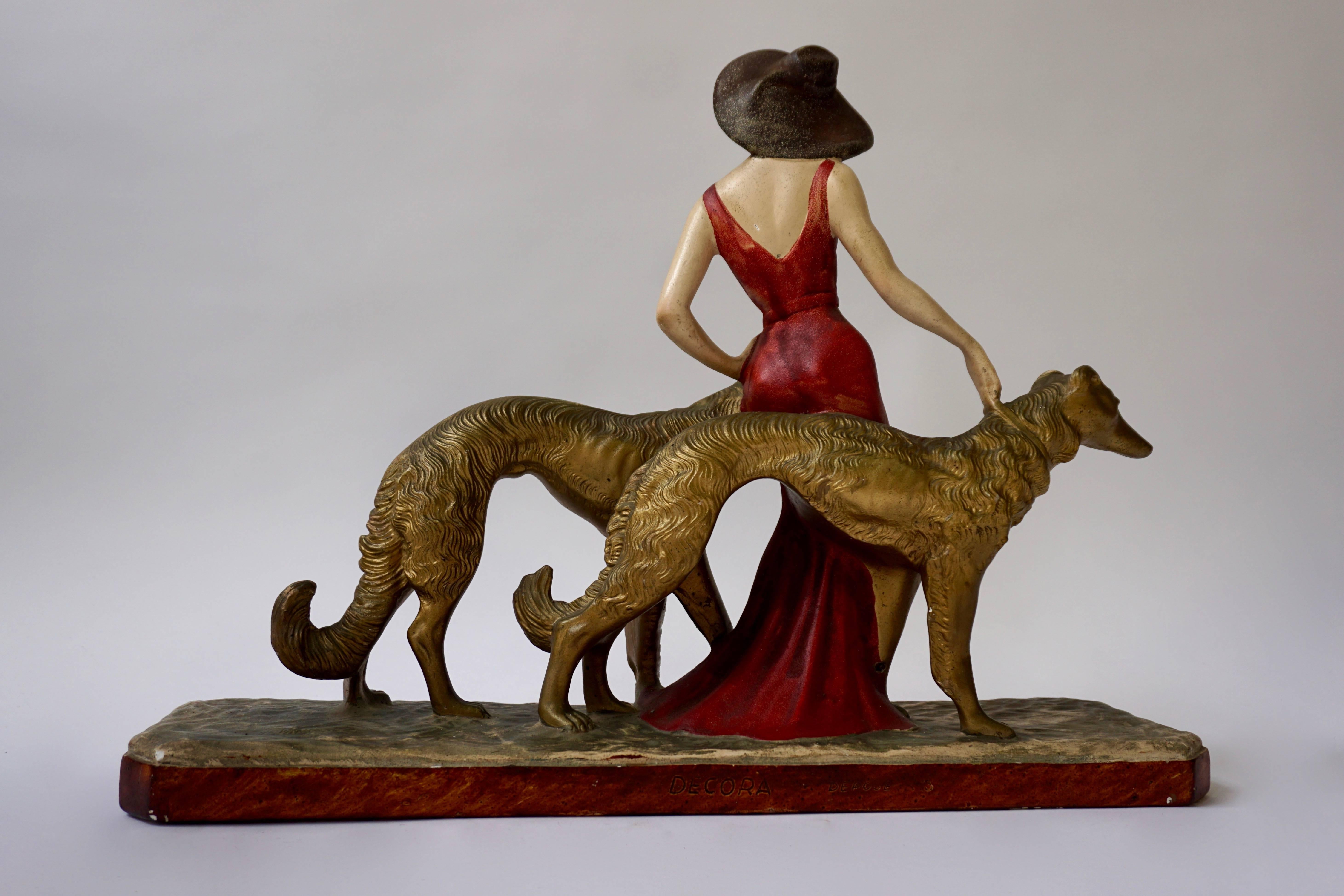 A painted plaster Art Deco figure of a lady walking her two greyhounds, circa 1930.