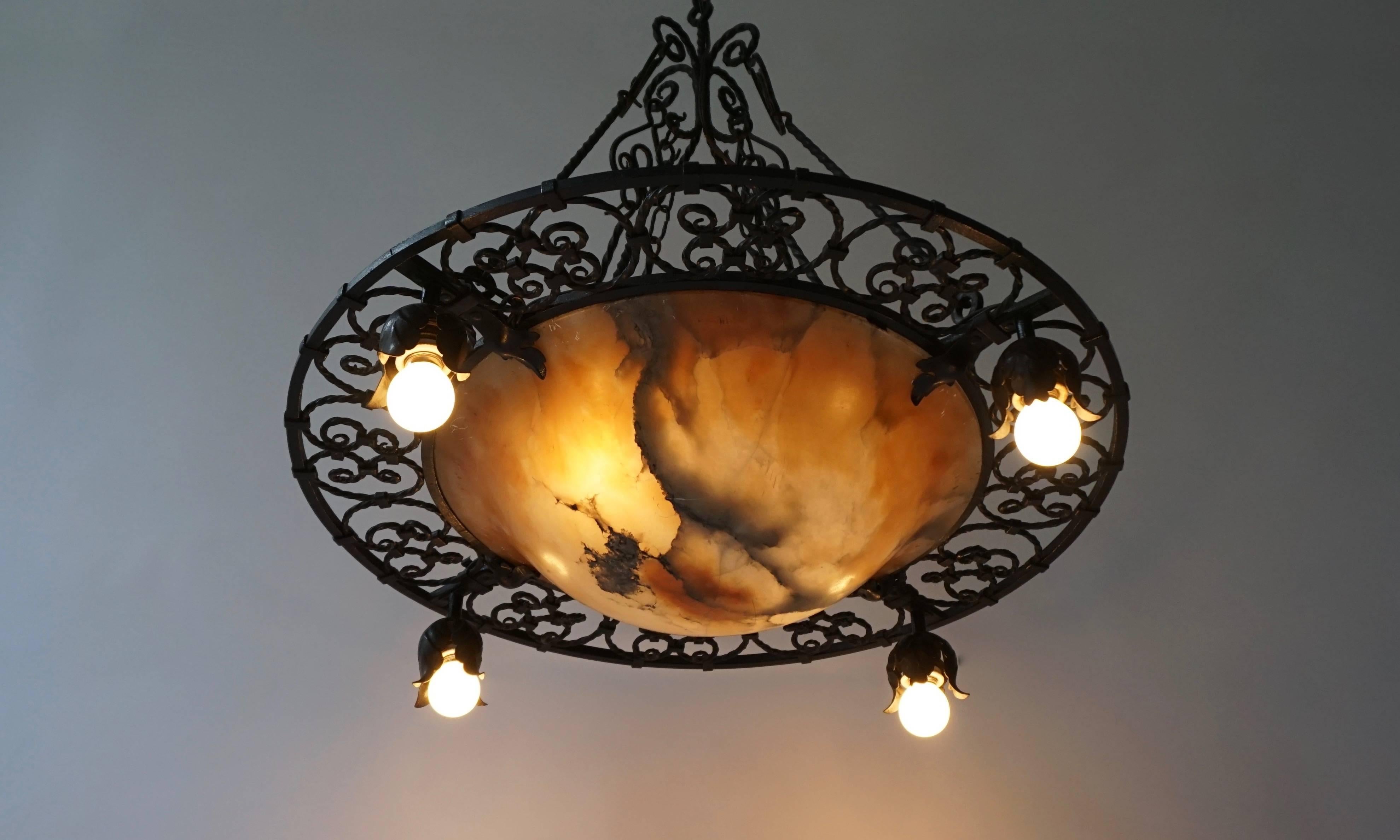 A wrought iron and alabaster Art Deco chandelier of typical shape, with four exterior lights hanging from flower bud sockets and additional lighting from within through the nicotine colored alabaster for atmosphere.
Diameter: 70 cm.
Heigth: 75