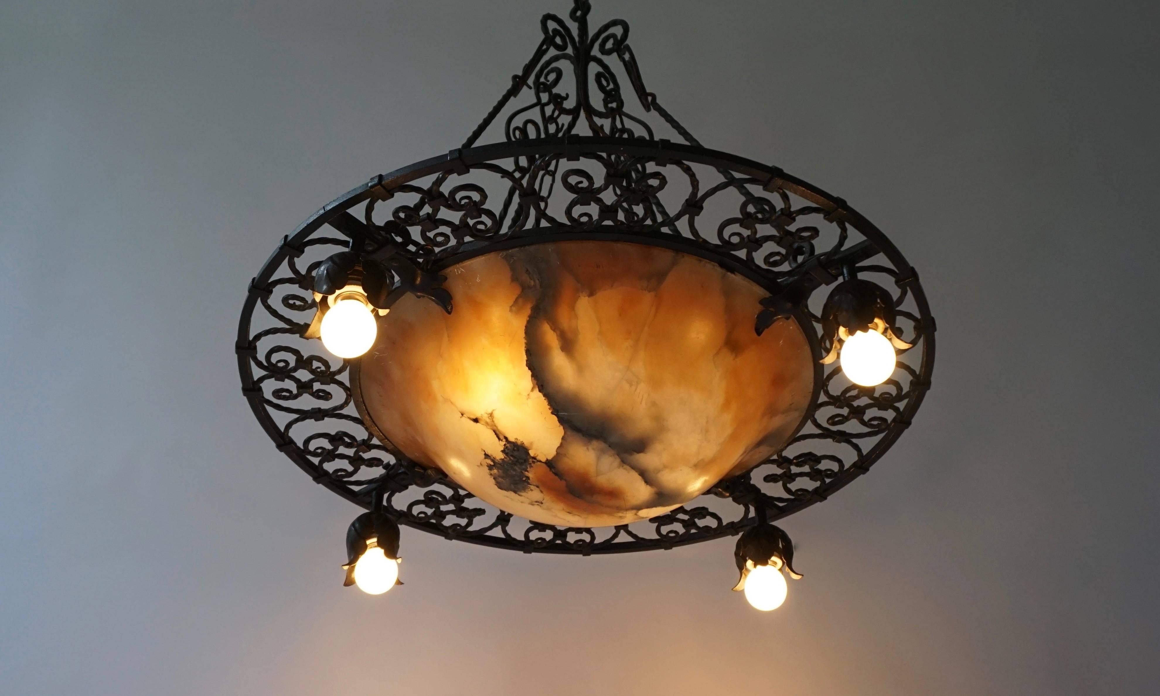 Un lampadario Art Deco in ferro battuto e alabastro dalla forma tipica, con quattro luci esterne appese a prese a bocciolo e un'illuminazione aggiuntiva dall'interno attraverso l'alabastro color nicotina per creare atmosfera.
Diametro: 70