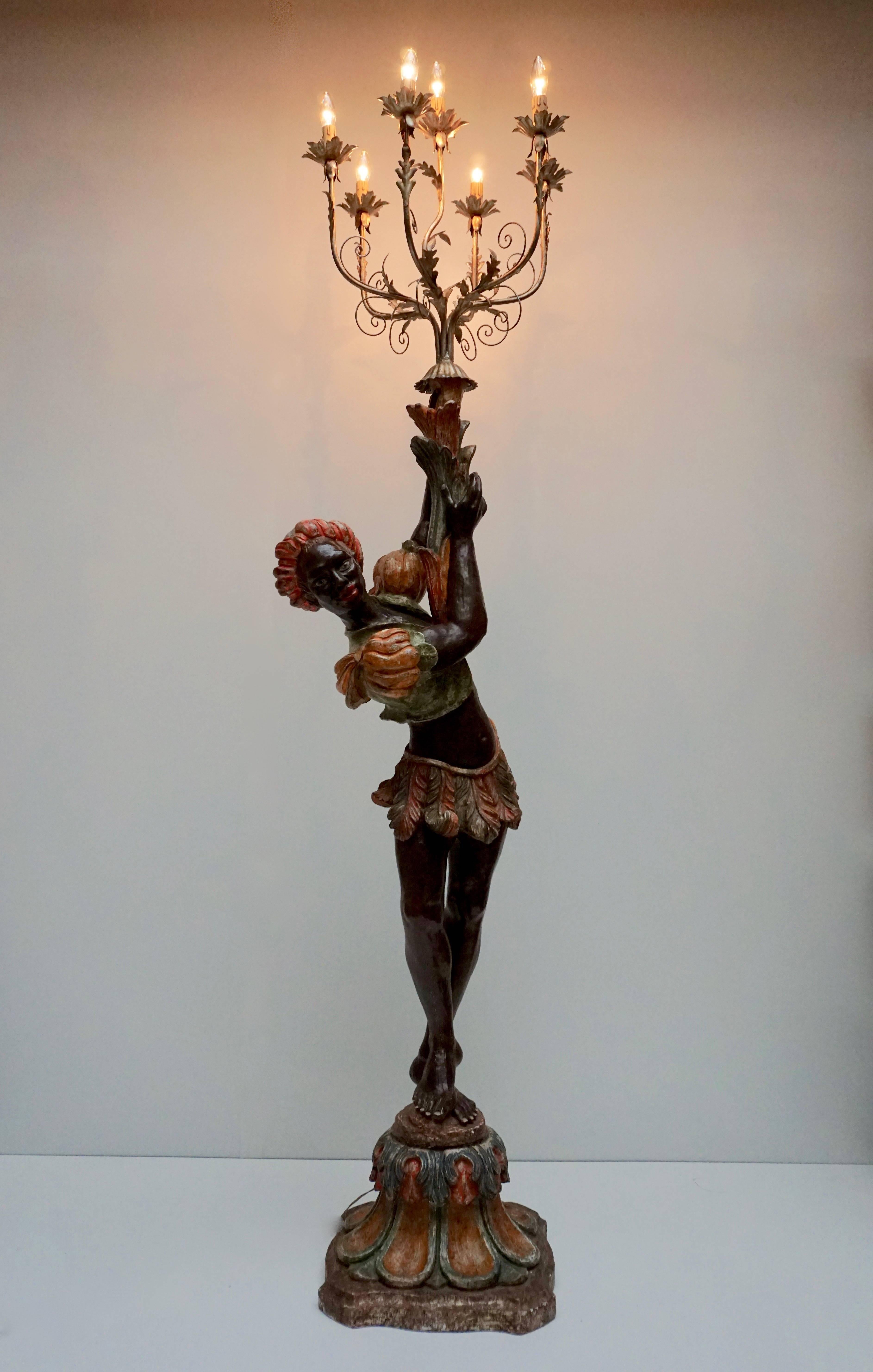 This is an exquisite decorative Venetian style candelabra floor lamp.
The figure are on decorative wooden stand and holds a large candelabra above its head with seven candle light bulbs. 

Dimensions in cm: Height 212 cm x width 50 cm x depth