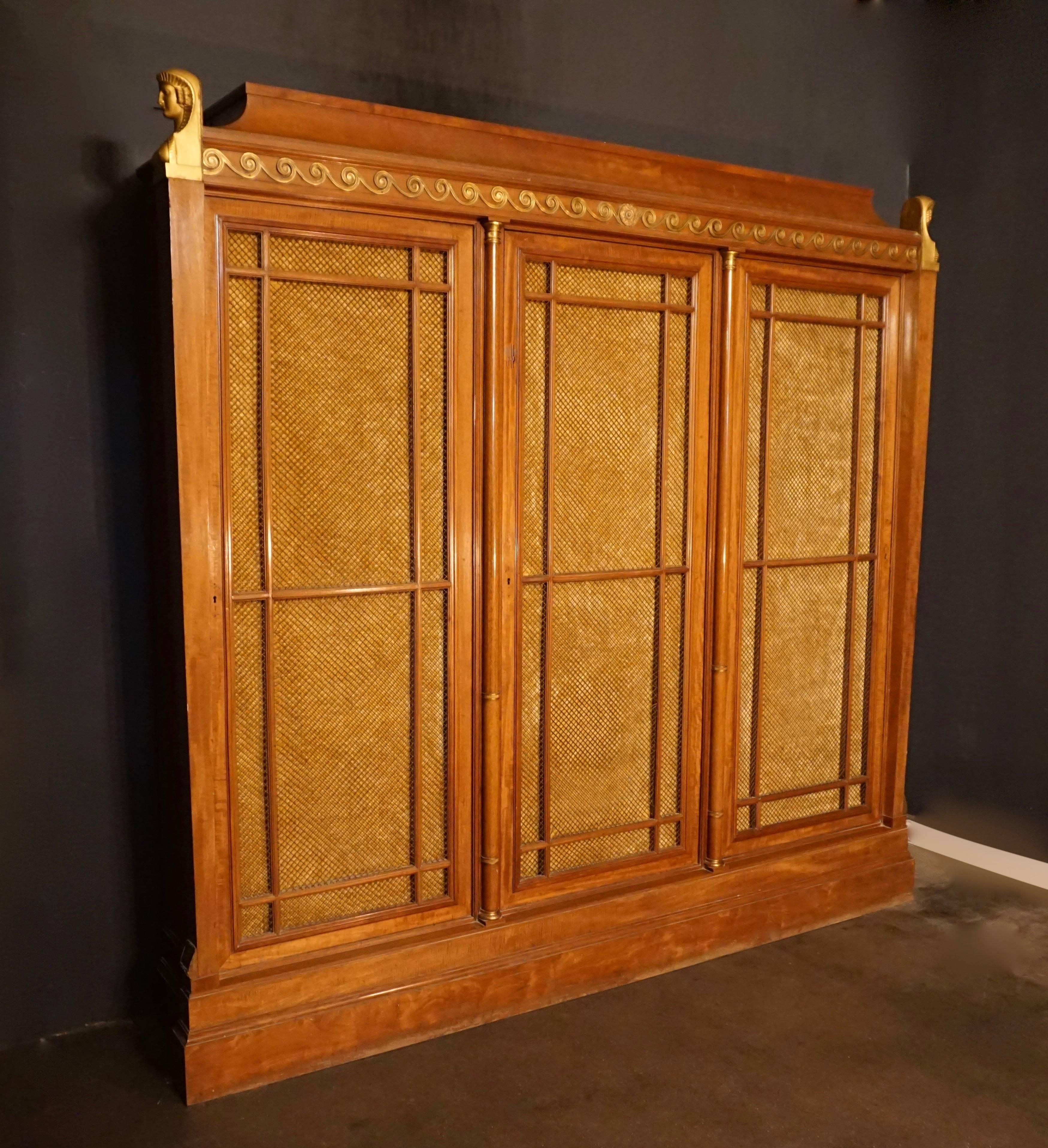 A rare and magnificent neoclassical mahogany three door bookcase dating to the second half of the 19th century.
 
Resting on a large plinth, the bookcase has three large frame doors with parallel detached moldings over a metal trellis work, backed