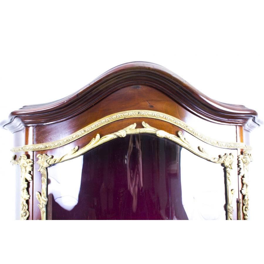 Il s'agit d'une superbe vitrine ancienne en acajou Vernis Martin, de style Louis XV, datant d'environ 1880, avec une exquise décoration peinte à la main et de superbes montures en bronze doré.

Le plateau présente des côtés en verre serpentin avec