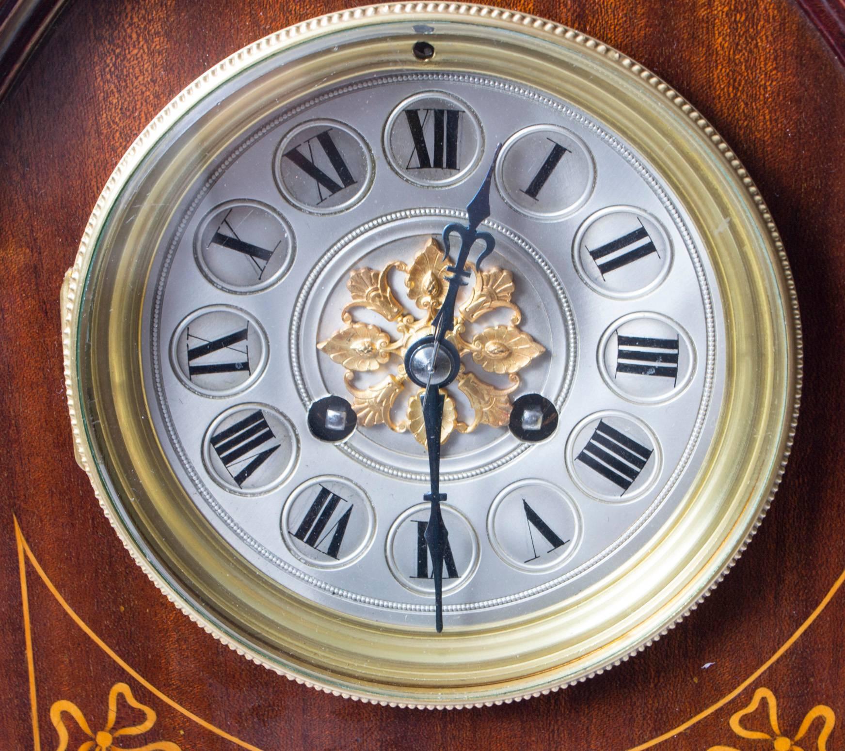 A delighful French marquetry inlaid mahogany lancet-top mantel clock, circa 1900 in date.

With brass and silvered concave dial, Roman chapter ring and gilt rosette centre fronting an eight day spring driven French movement with gong strike..

The