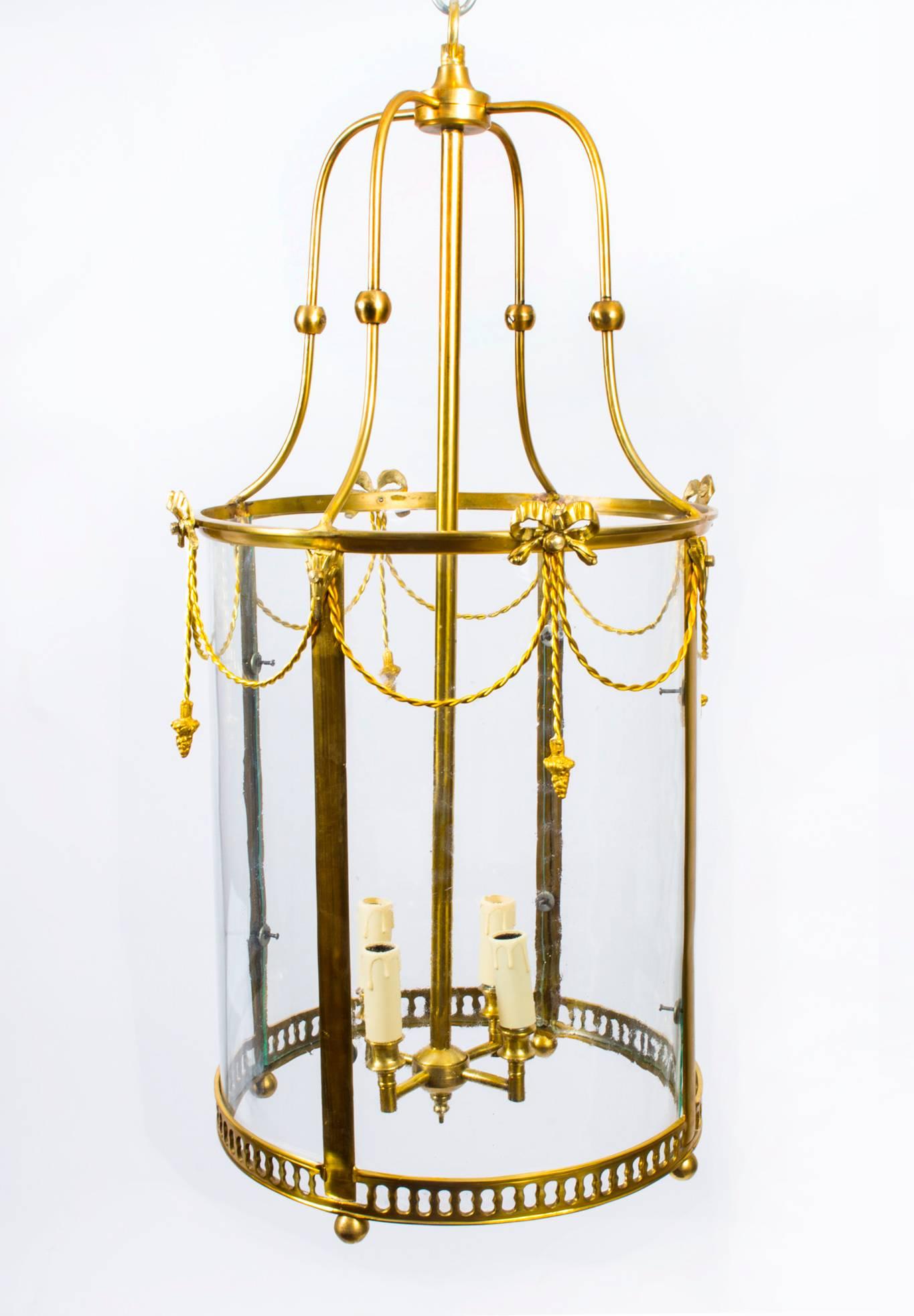 This is a stylish hall or entrance lantern made of solid brass with glazed sides in the elegant Sheraton style, dating from the last quarter of the 20th century.

The four light lantern's main frame has upper tasselled inserts, acorn decorative