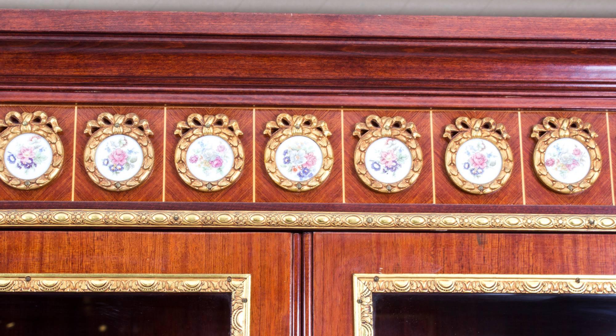 This is a superb vintage ormolu and porcelain mounted mahogany, burr walnut and marquetry bow front vitrine in the Louis XV transitional style, dating from the second half of the 20th century.

It bears the impressed stamp of the renowned cabinet