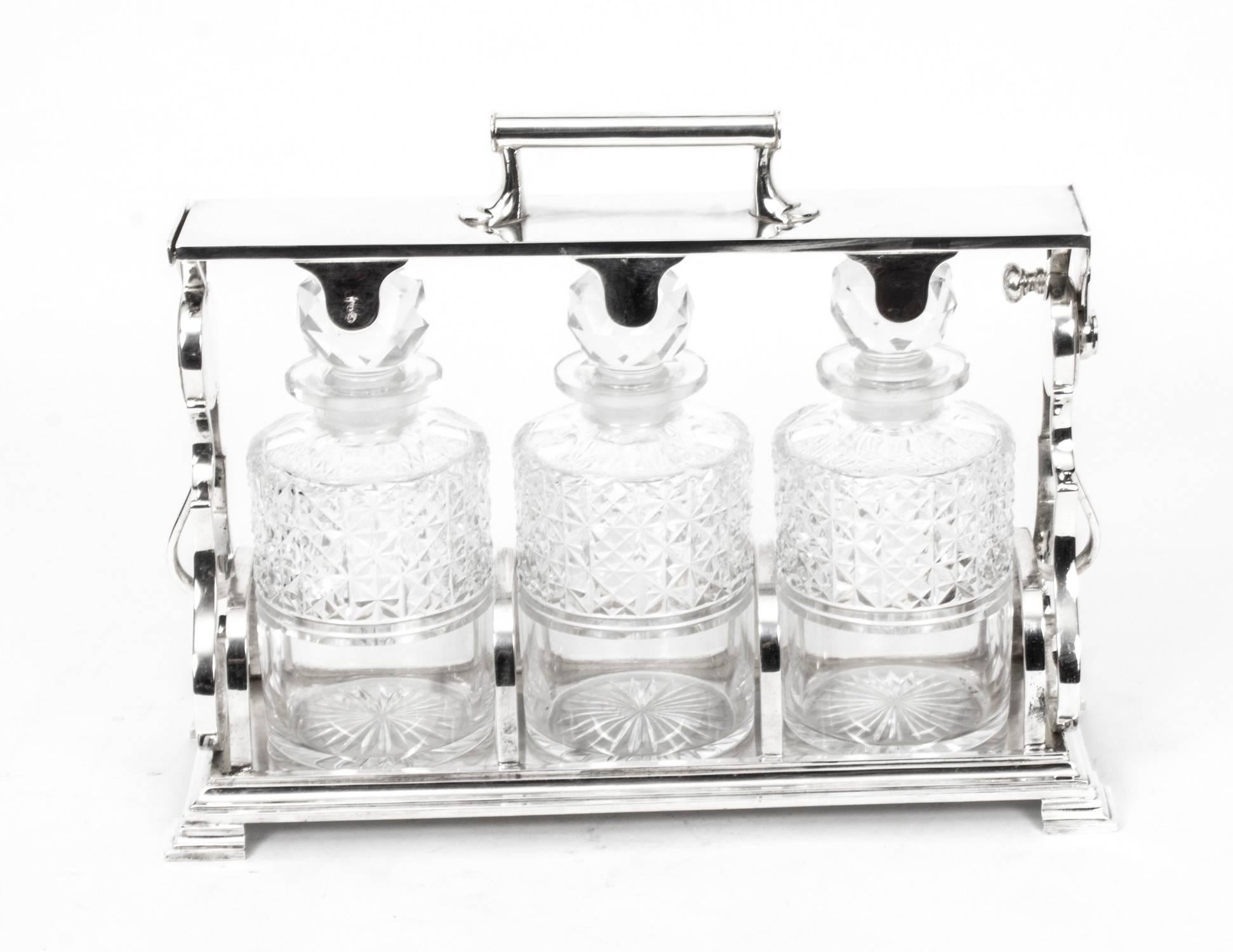 An attractive Victorian English silver plated three bottle tantalus set, with unique locking mechanism, fitted with three hand cut crystal circular decanters and stoppers, on a rectangular base and raised on bun feet, maker: Norman & White,
