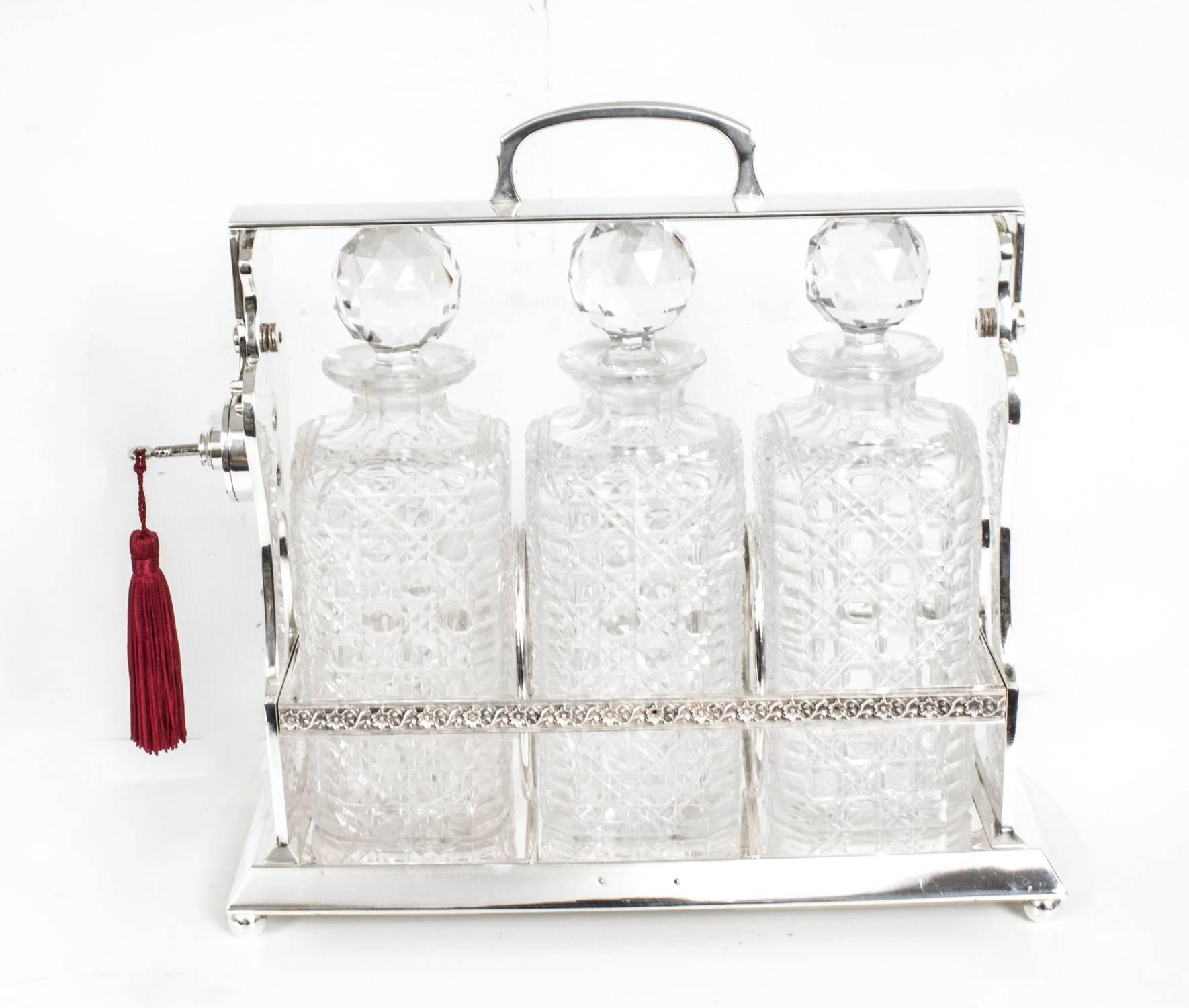 An attractive Victorian "Betjemann" patent' silver plated three bottle tantalus set, with unique locking mechanism, fitted with three hand cut crystal hobnail and lozenge decorated square decanters and stoppers, on a rectangular base and