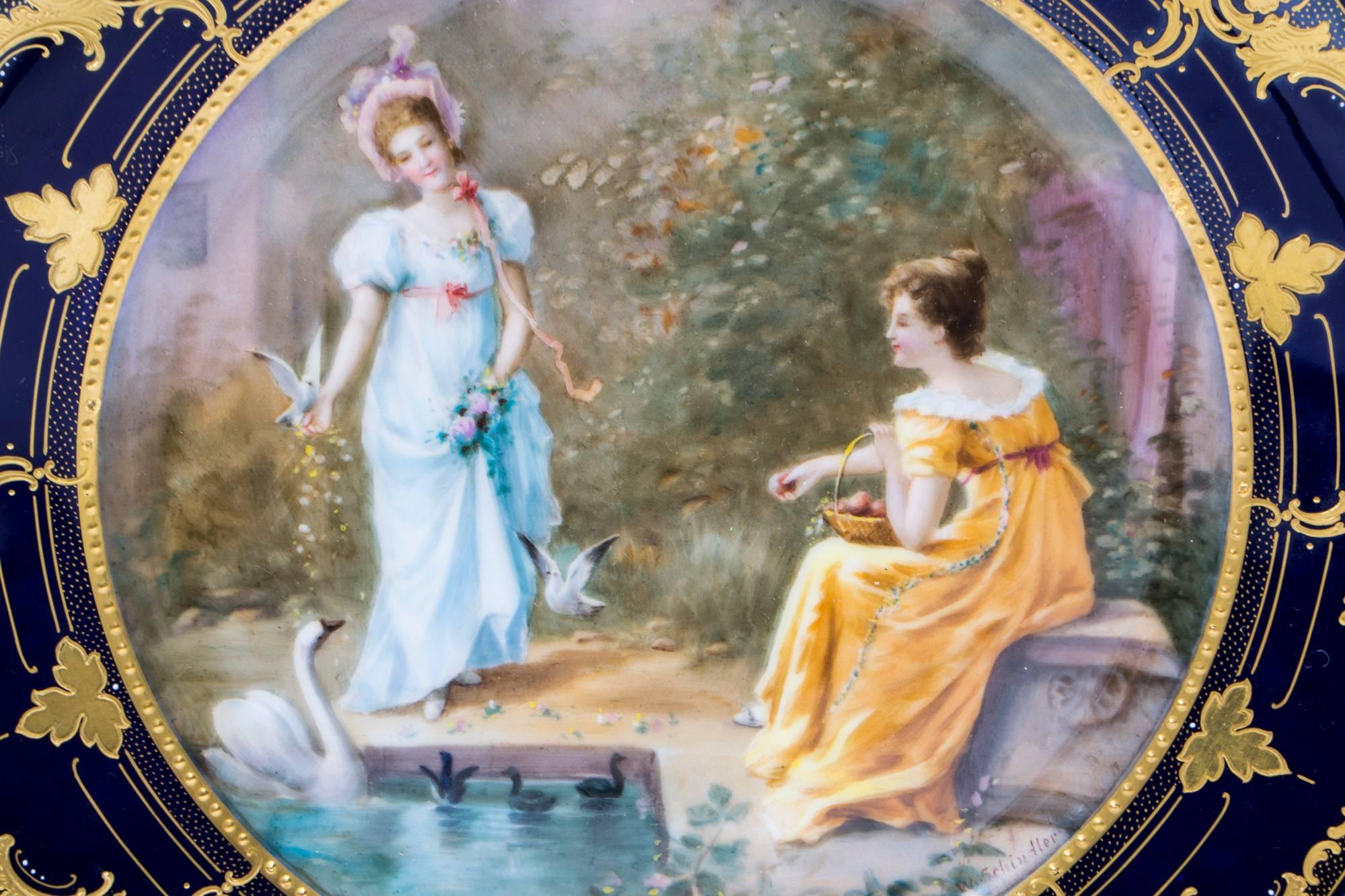 This is a wonderful antique Vienna porcelain cabinet plate, circa 1880 in date.

It is beautifully hand-painted with young women in a garden feeding a swan with her cygnets. It is signed W. Schindler, within a striking cobalt blue gilt decorated