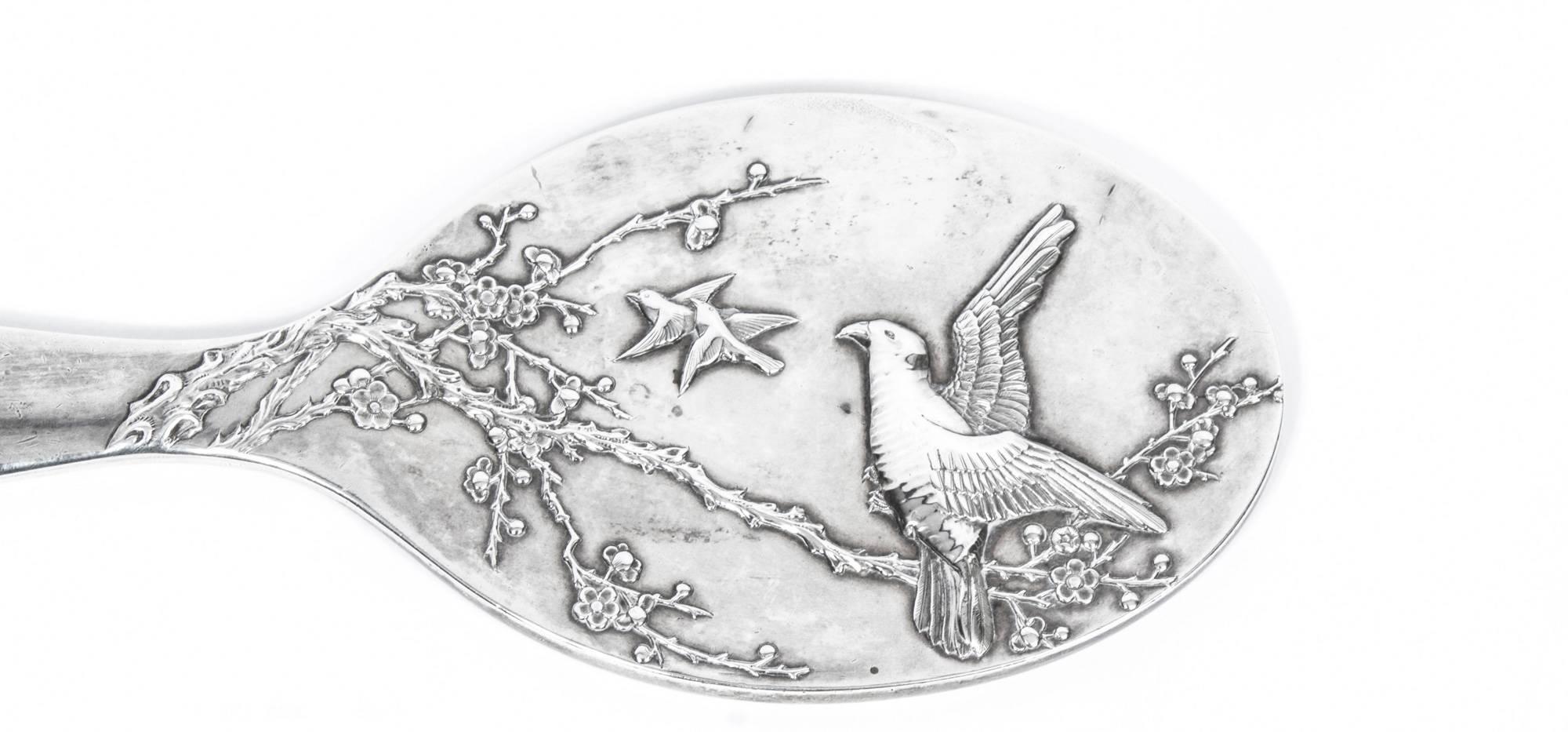 This is a wonderful antique Chinese silver export hand mirror, depicting in low relief three birds in flight above a blossom tree.

Bearing marks for the renowned Chinese silversmith Luen Hing, Shanghai, circa 1910.
It is a lovely object which