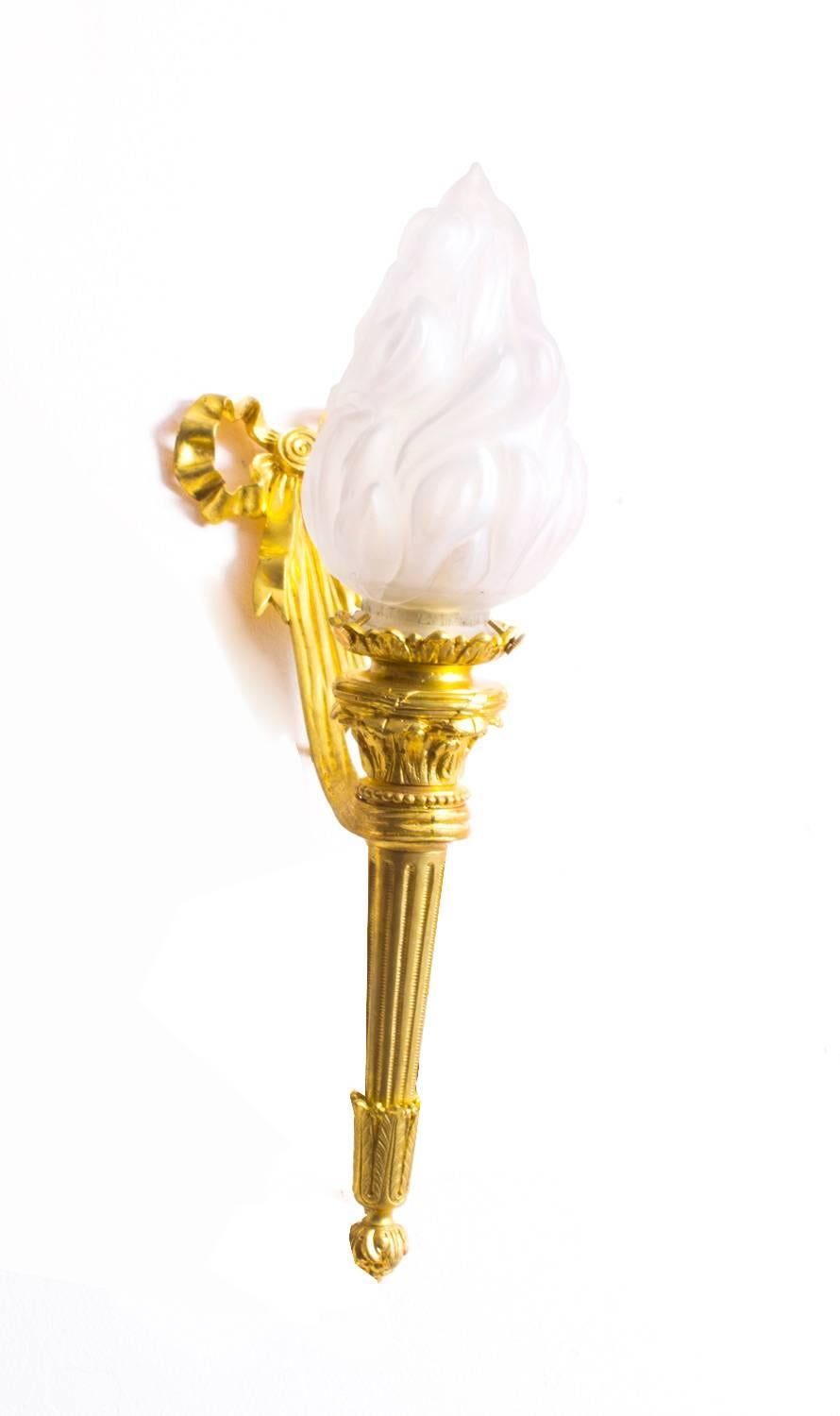 This is a superb pair of stylish French ormolu and glass flaming torch wall lights, circa 1920 in date.

Each has an ormolu ribbon backplate holding a torch at an angle with frosted glass torches, the quality and craftsmanship of these stunning