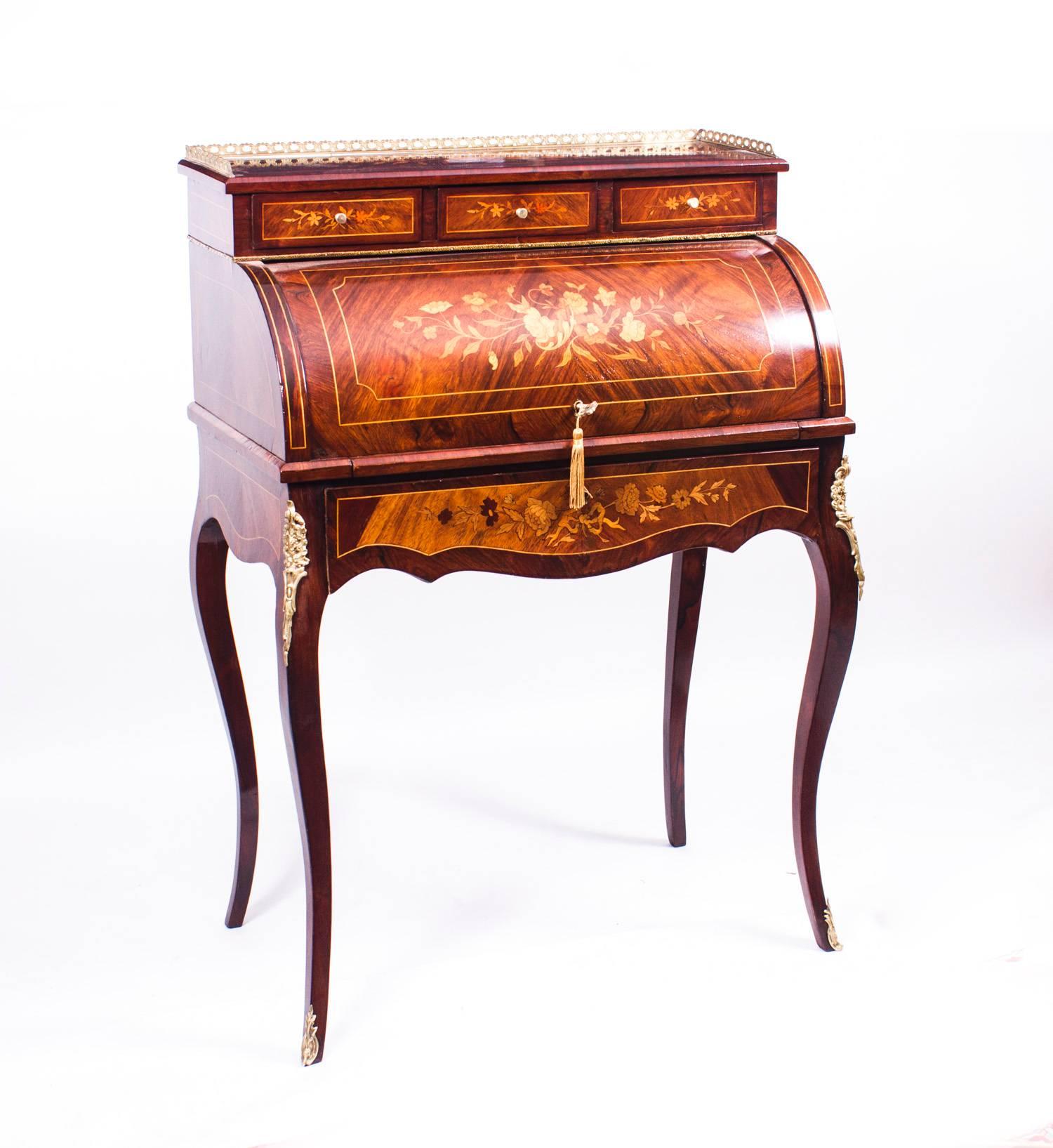 This is a gorgeous antique French Louis XV rosewood and marquetry bureau a' cylindre, circa 1870 in date, with stunning floral marquetry decoration and ormolu mounts.

It has a pierced brass three quarter gallery above three small frieze drawers