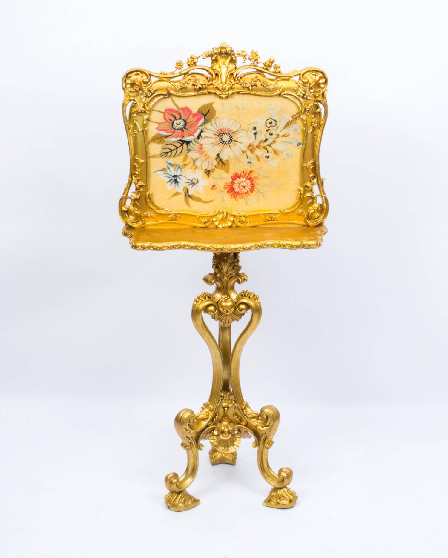 This is a beautiful English antique Victorian giltwood screen, circa 1850 in date. 

It features a woolwork floral tapestry with a shelf to the front and stands on elaborate Rococo supports.

It bears the makers label for 'John Tozer, Carver,
