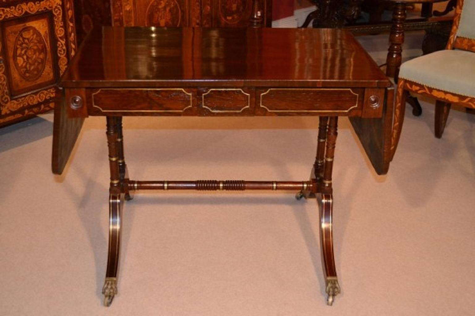 This is a sublime antique Regency rosewood sofa table circa 1820 in date. 

It is crafted from beautiful rosewood which has been masterfully inlaid with brass, and has two capacious drawers. It stands on a twin base with stretcher and the legs