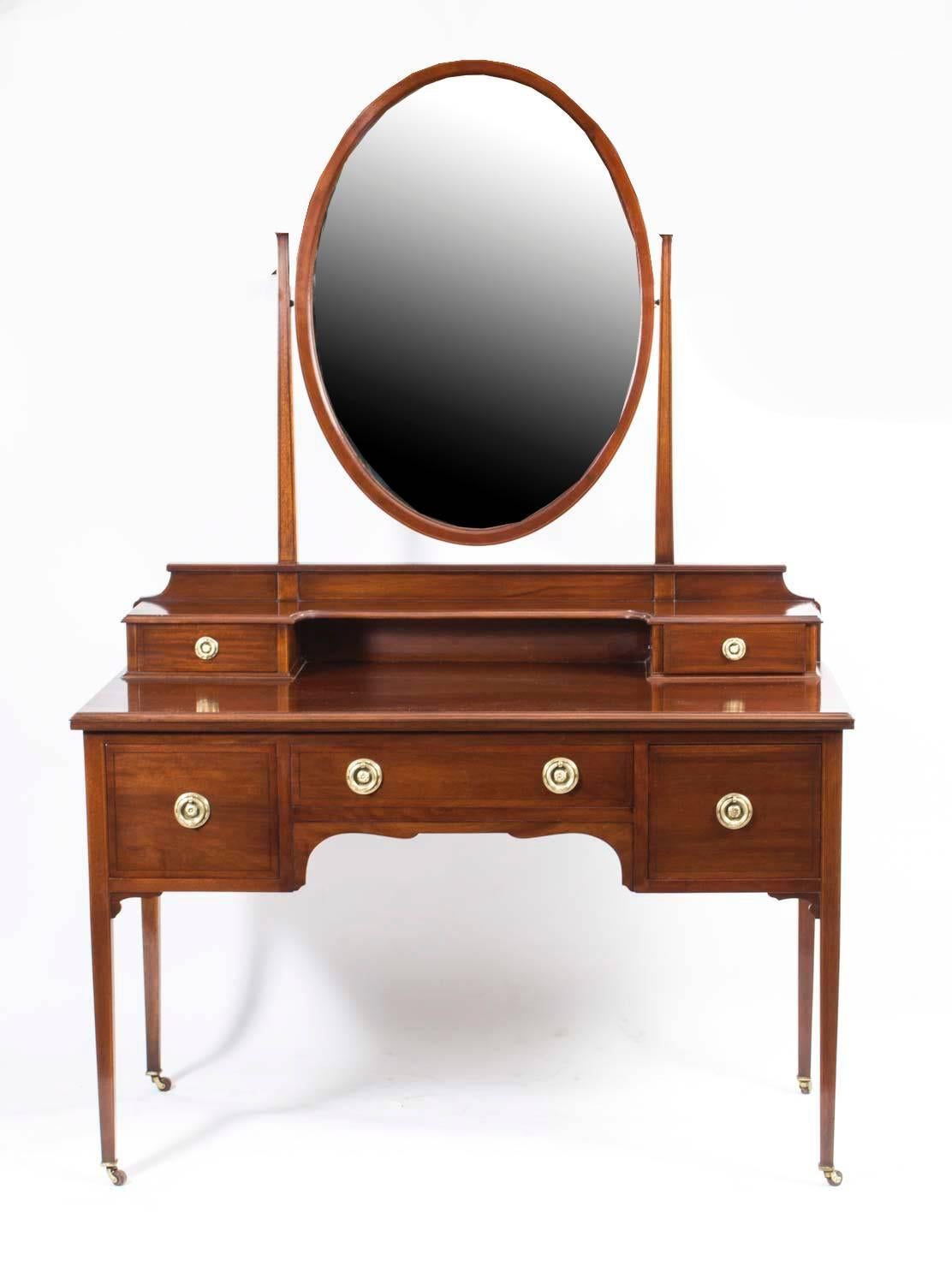 This is a totally fabulous antique inlaid mahogany dressing table with adjustable mirror, circa 1900 in date.

The top surmounted by an oval shaped mirror with square column supports. It has two small trinket drawers below the mirror, over three