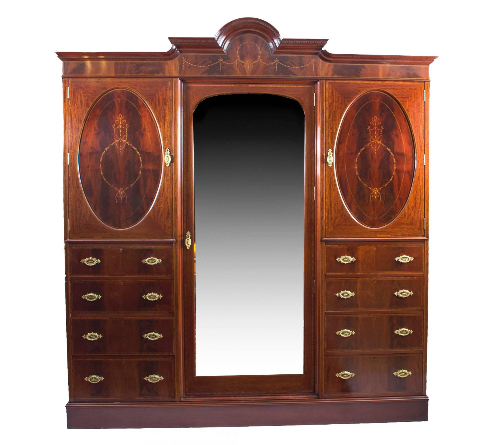 This is a lovely antique English inlaid flame mahogany triple wardrobe, circa 1880 in date.

It has been accomplished in the most beautiful 'flame mahogany' with fabulous satinwood banding and superb inlaid decoration comprising ribbon tied laurel