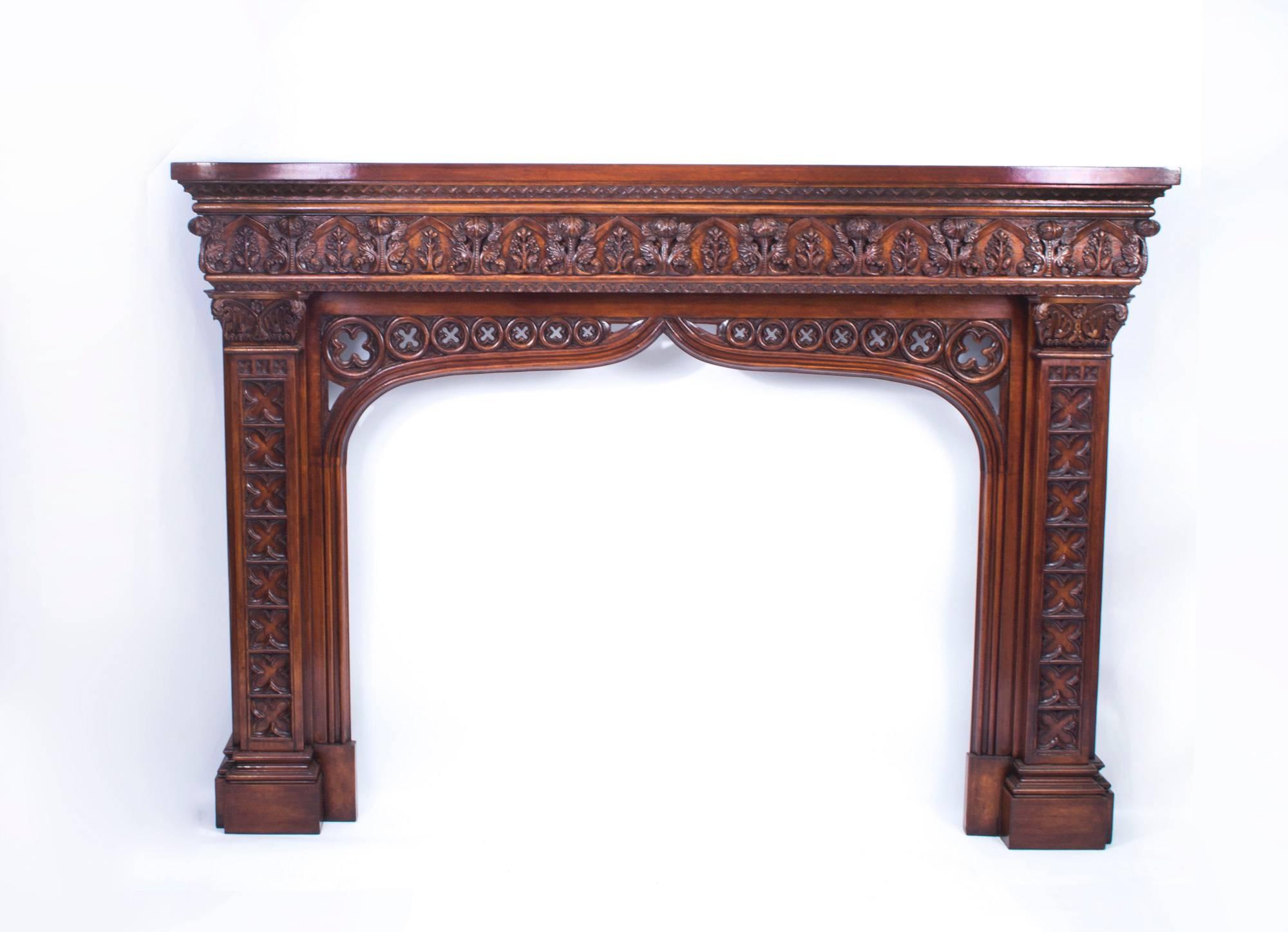 This is a large impressive and profusely carved pair of solid mahogany chimney pieces in the neo Gothic style of A. W. N Pugin, dating from the early 20th century.

Each has a contoured shelf over Puginesque foliate carved decoration with an open