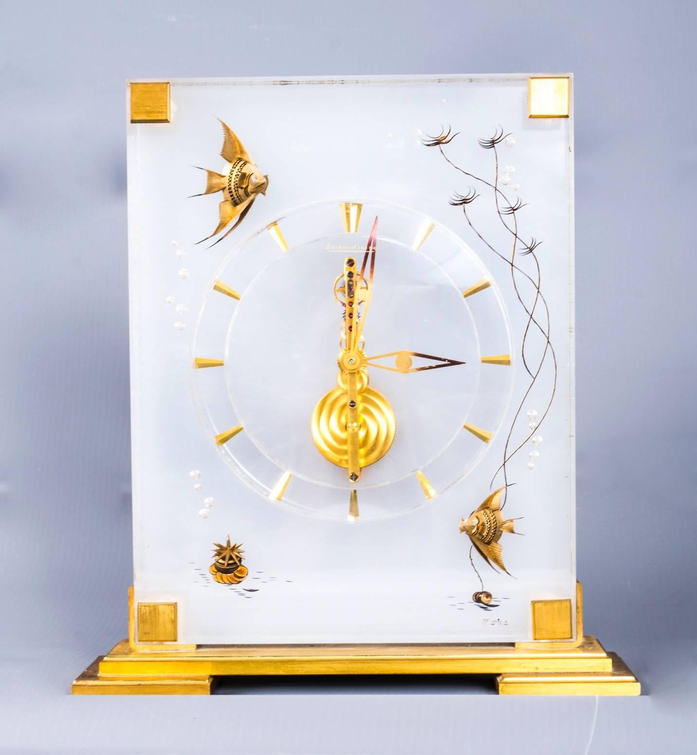 This is beautiful and very decorative vintage Jaeger-LeCoultre marina desk clock dating from the early 1960s.

The beautiful polished gilt brass and Lucite case decorated with delightful angel fish designs, a baguette movement and the original