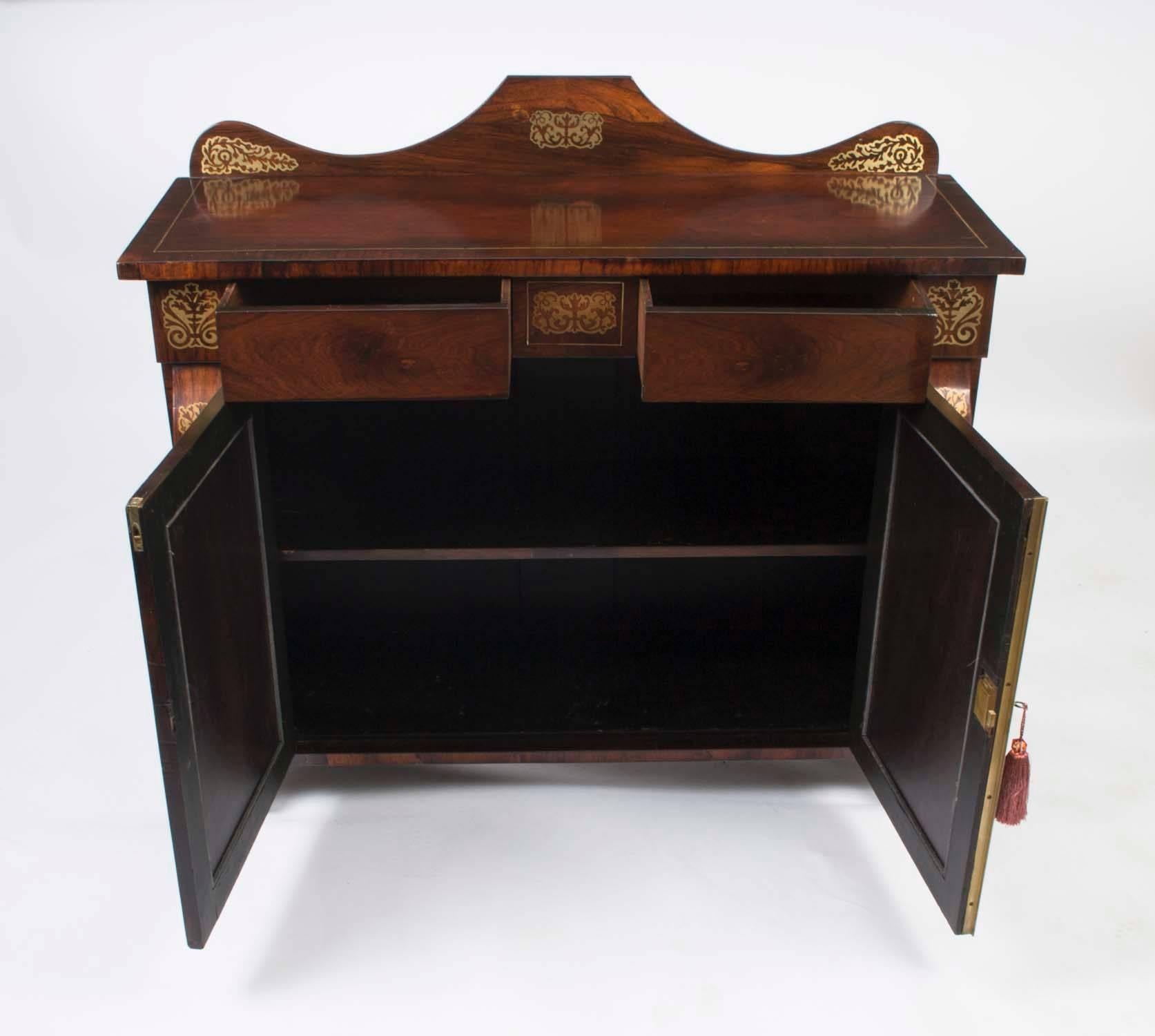 This is an elegant antique Regency period brass inlaid chiffonier, circa 1820 in date.

This magnificent cabinet has an arched shaped back and features a pair of grilled doors with powder pink silk linings that open to reveal a cupboard with a