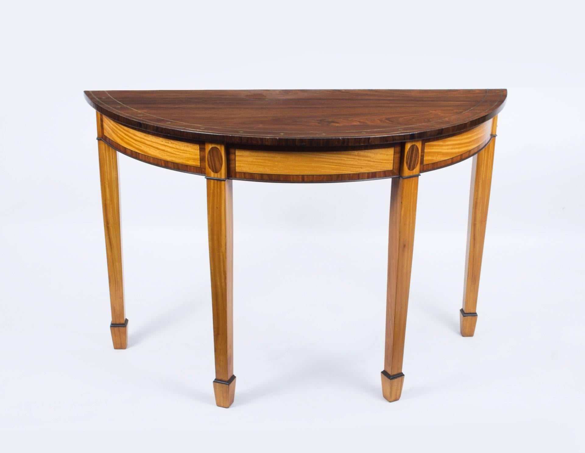 This is a rare antique pair of English Regency style demilune console tables, circa 1900.

They feature elaborate brass inlaid decoration around the tops and are made from two woods which compliment themselves: Rosewood and satinwood.

There is