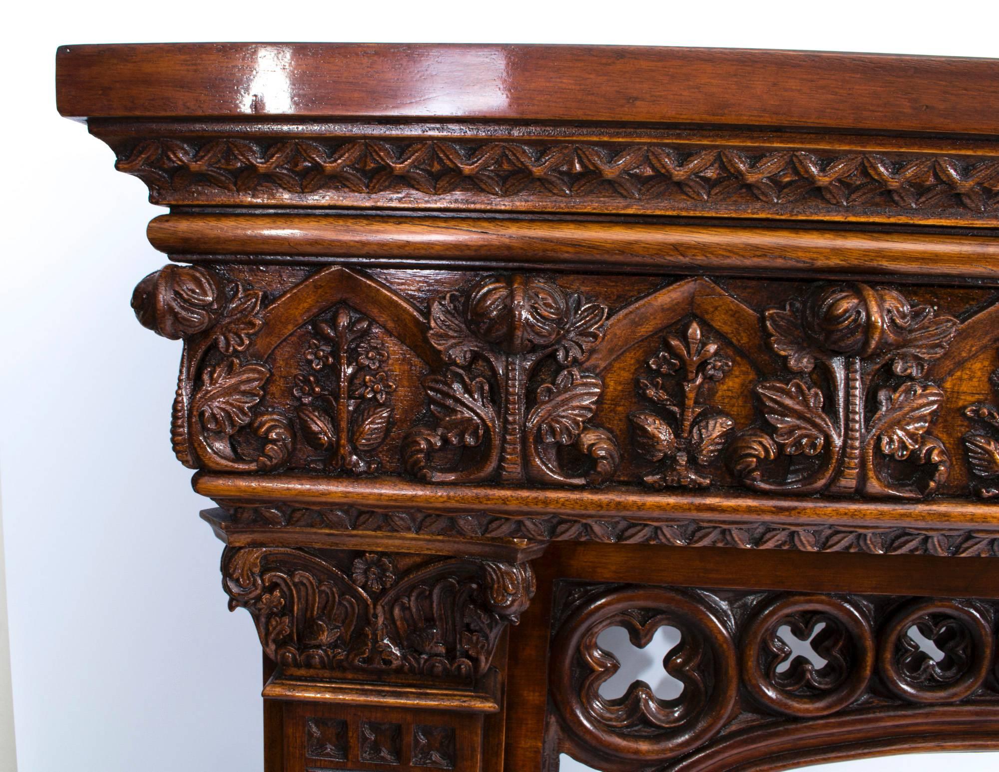 This is a large impressive and profusely carved solid mahogany chimney piece in the neo-Gothic style of A. W. N Pugin, dating from the early 20th century.

It has a contoured shelf over Puginesque foliate carved decoration with an open clover leaf