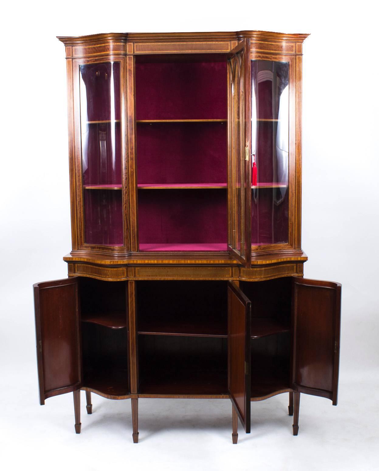 A superb antique English Edwardian mahogany serpentine display cabinet, circa 1900 in date, of the very highest quality, with inlaid decoration, typical of Edwards and Roberts furniture.

The top part has a large central door with astragal glazing